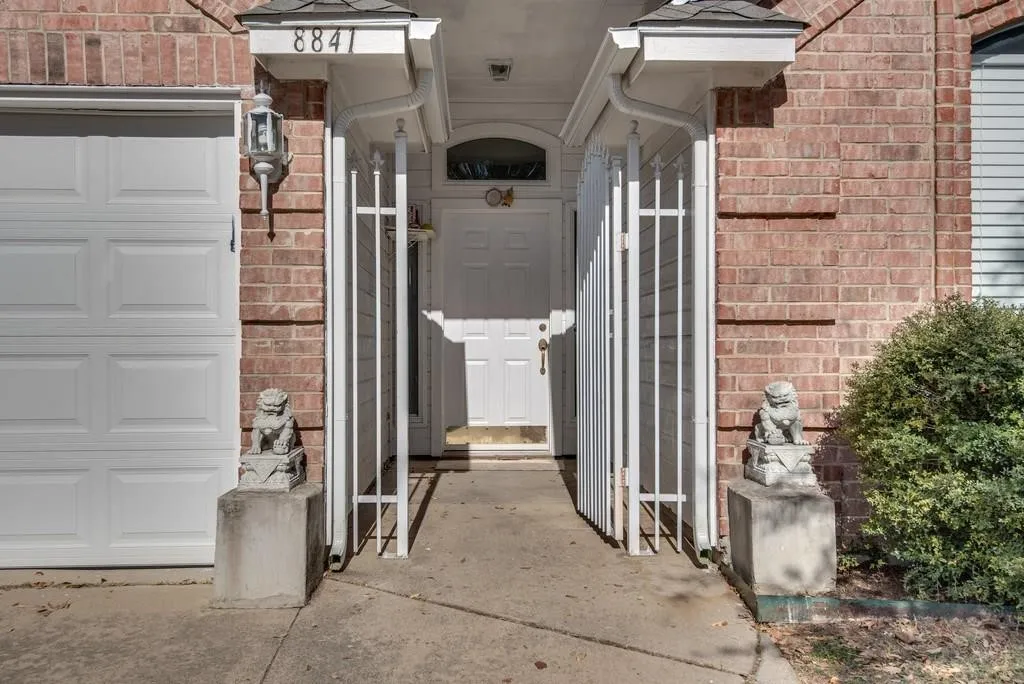 Brick exterior featuring a white paneled garage door, a white entry door with an arched transom, and white decorative security gates
