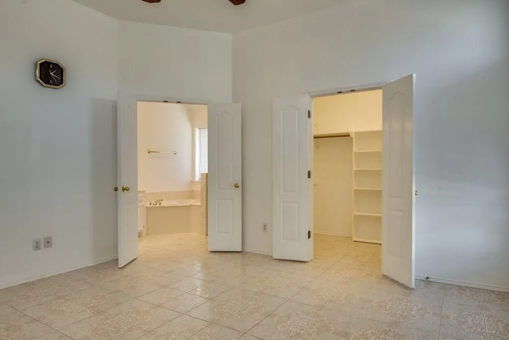 Spacious room featuring tile flooring, a dual-door entry to a closet with built-in shelving, and a separate dual-door entry to a full bathroom with a built-in tub
