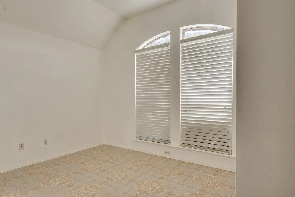 Room featuring an arched window, two rectangular windows with blinds, vaulted ceilings, and patterned tile flooring