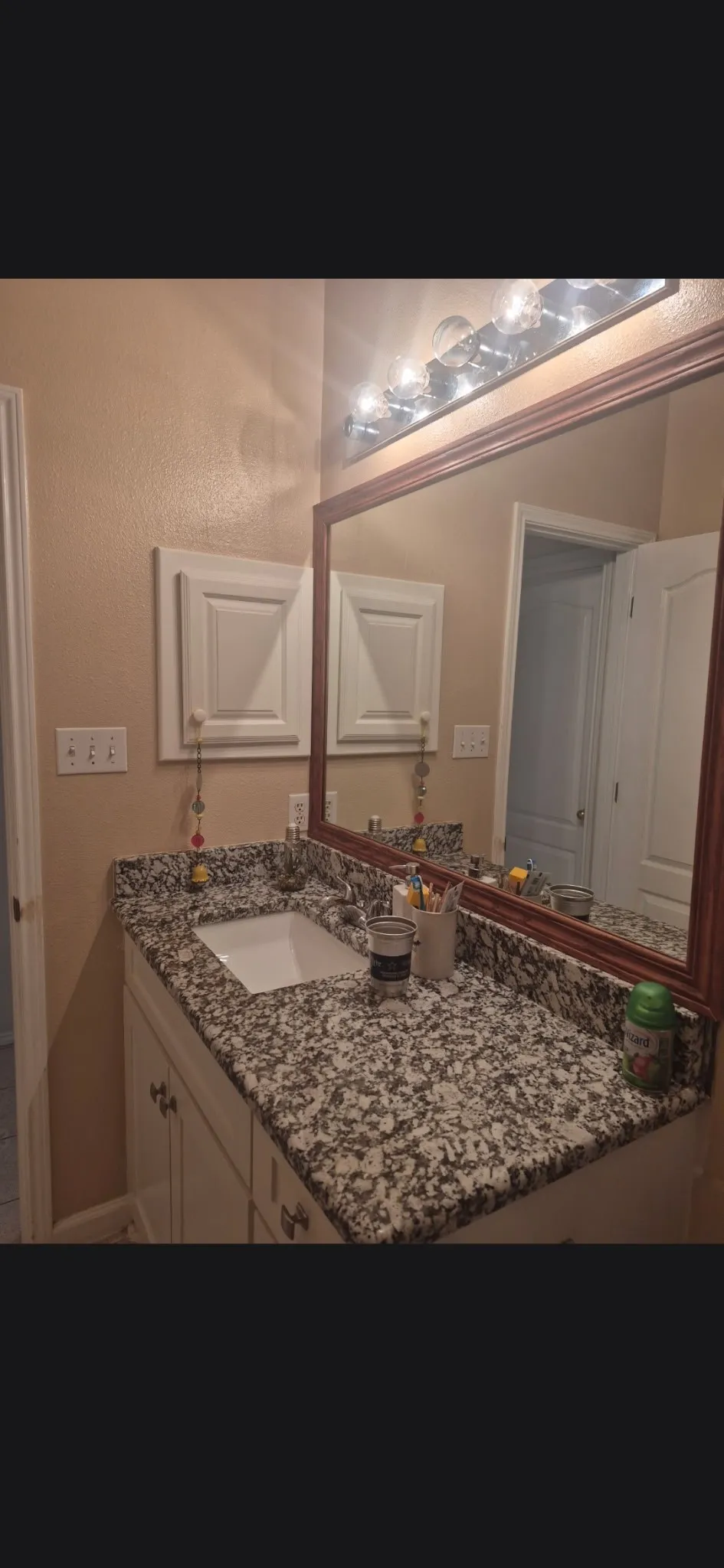 Granite countertop vanity with integrated sink, white cabinetry, framed mirror, and upper wall-mounted storage cabinets