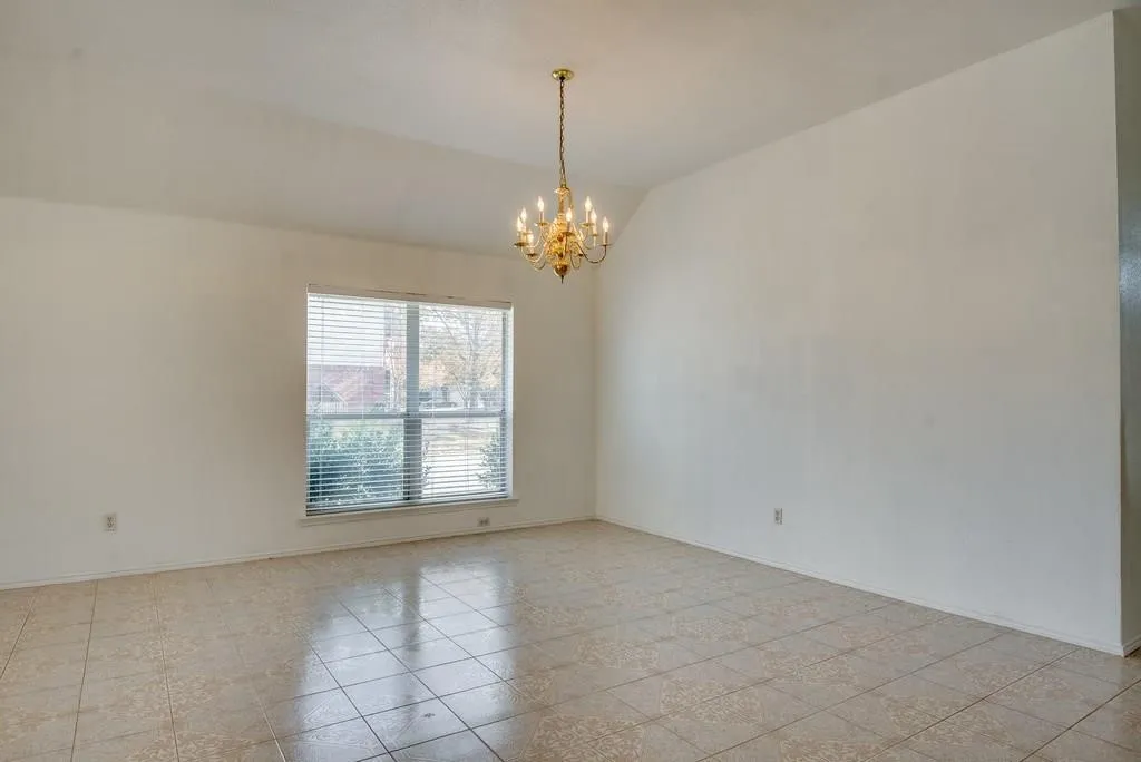 Spacious room featuring vaulted ceilings, a prominent window with blinds, and tiled flooring