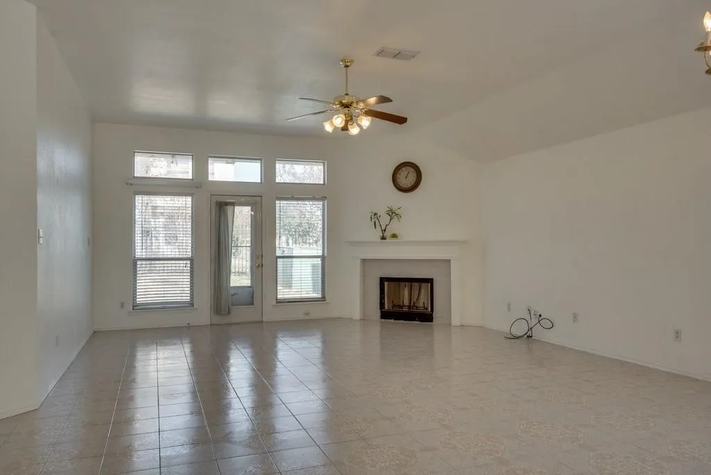 Living area featuring vaulted ceilings, tile flooring, a built-in fireplace with mantle, and a rear door with surrounding windows