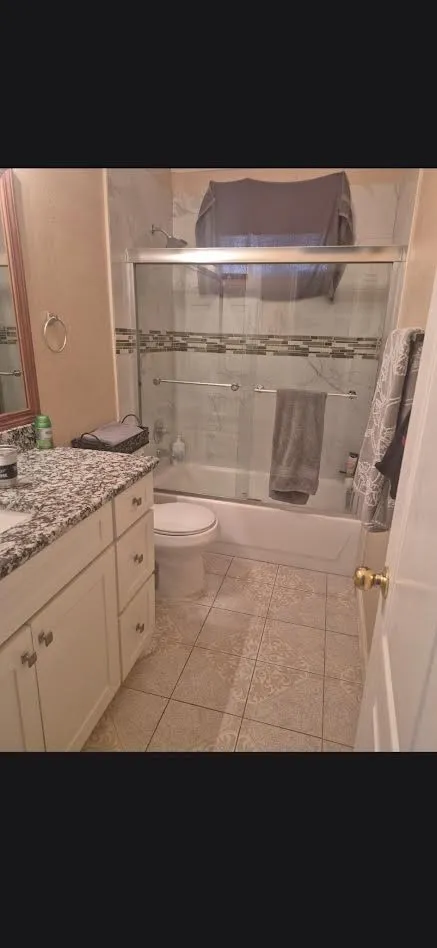 Full bathroom featuring a white vanity with a speckled countertop, a shower-tub combination with a sliding glass door, and patterned tile flooring