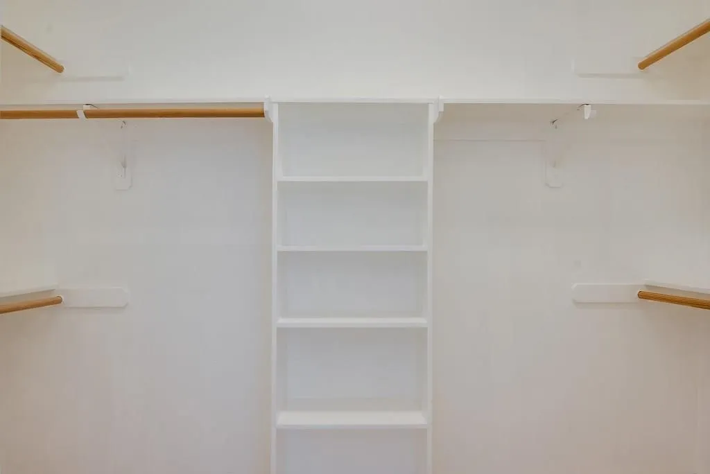 Custom closet system featuring white shelving and natural wood hanging rods