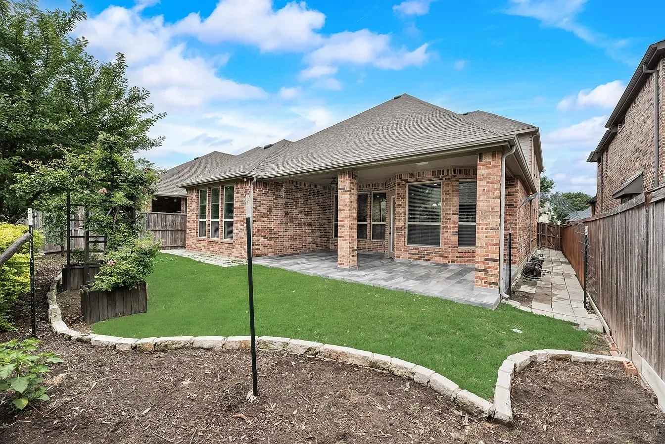 Brick exterior with covered patio, paver patio flooring, and a landscaped backyard featuring a retaining wall