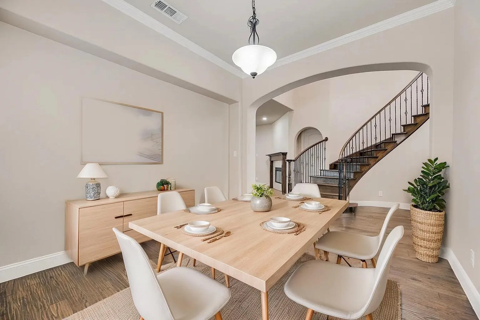 Hardwood-style flooring, arched doorways, crown molding, and an open spindle staircase with wrought iron balusters