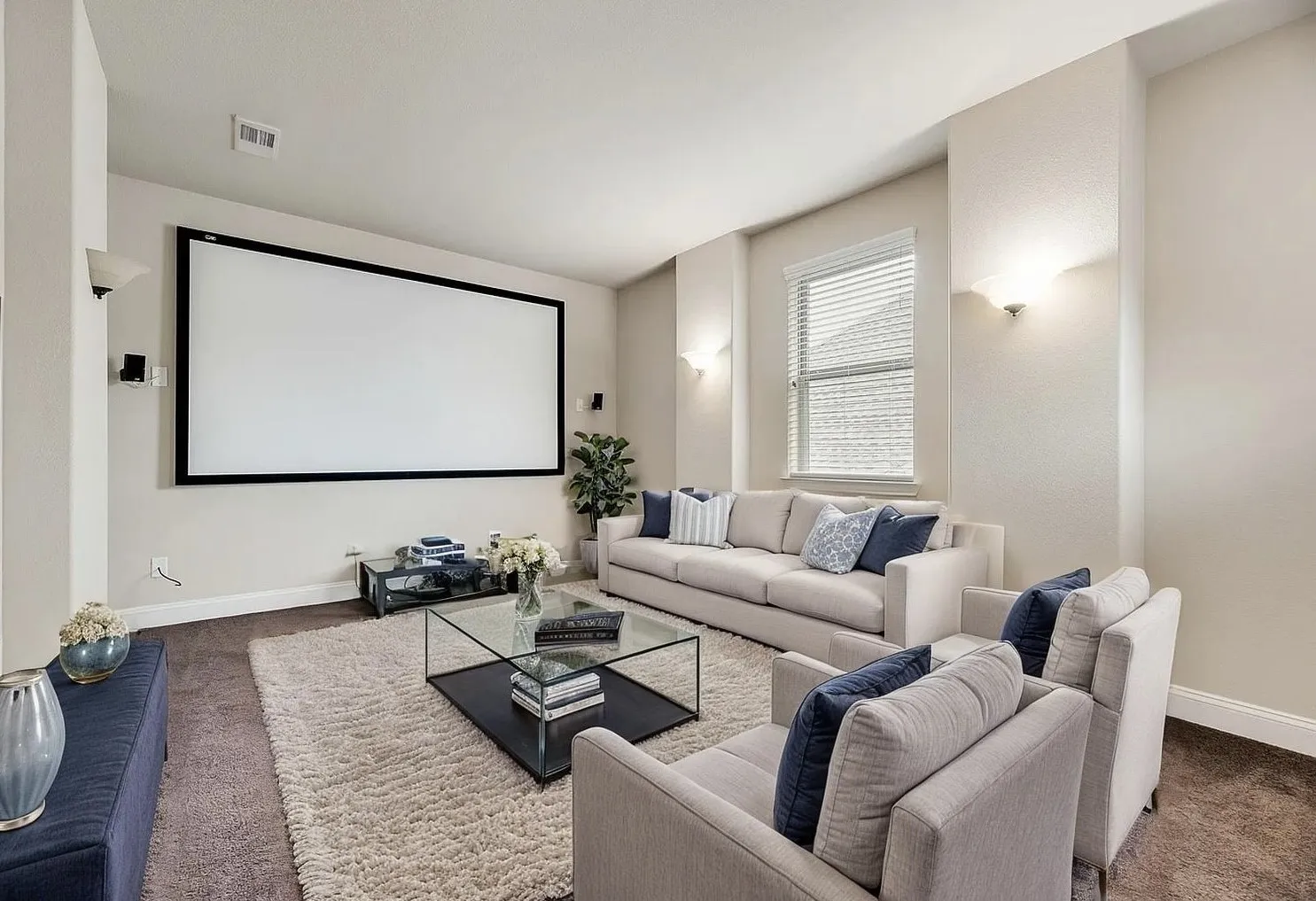 Large projection screen, recessed lighting, wall sconces, window with blinds, and built-in speakers
