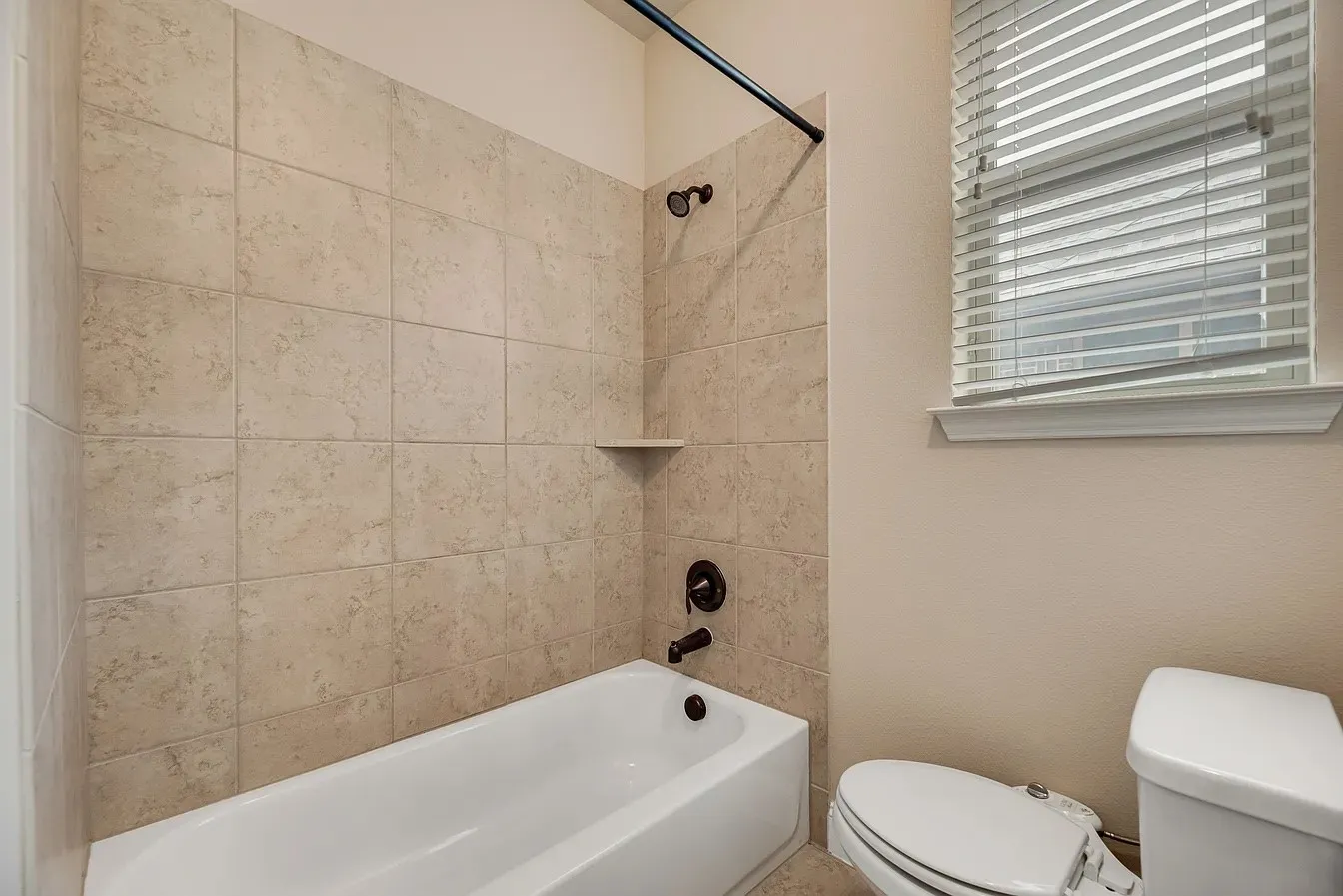 Bathroom featuring a white bathtub, beige tiled surround, and a corner shelf