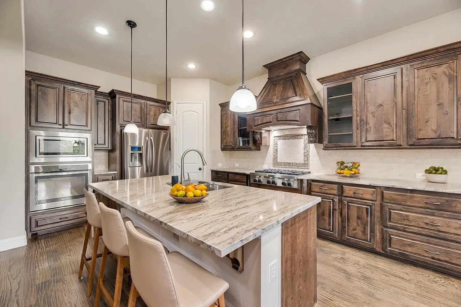 Expansive kitchen island with a stone countertop, wood-finish flooring, and pendant lighting