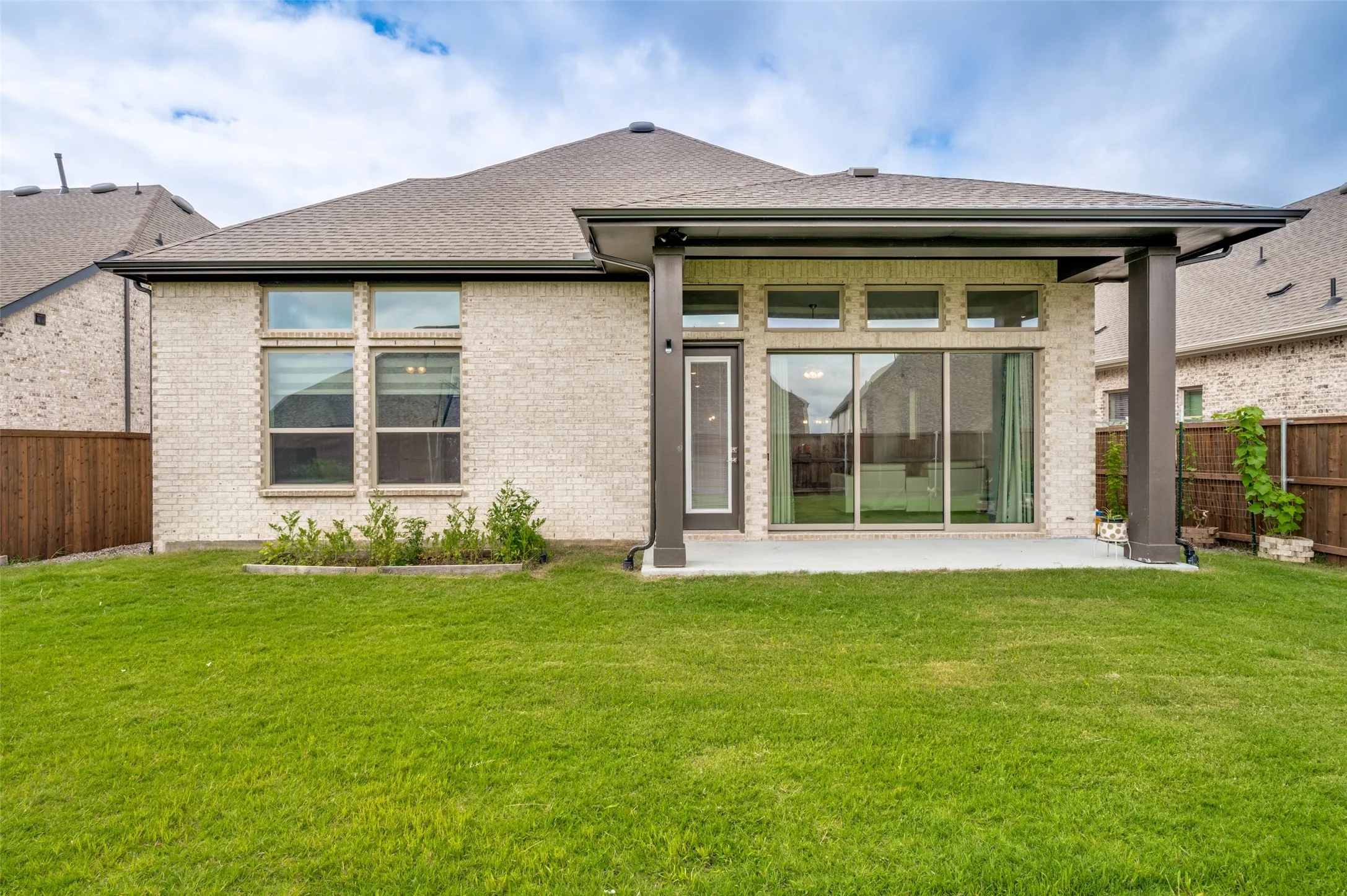 Expansive green lawn featuring a covered patio, large sliding glass doors, and a brick exterior