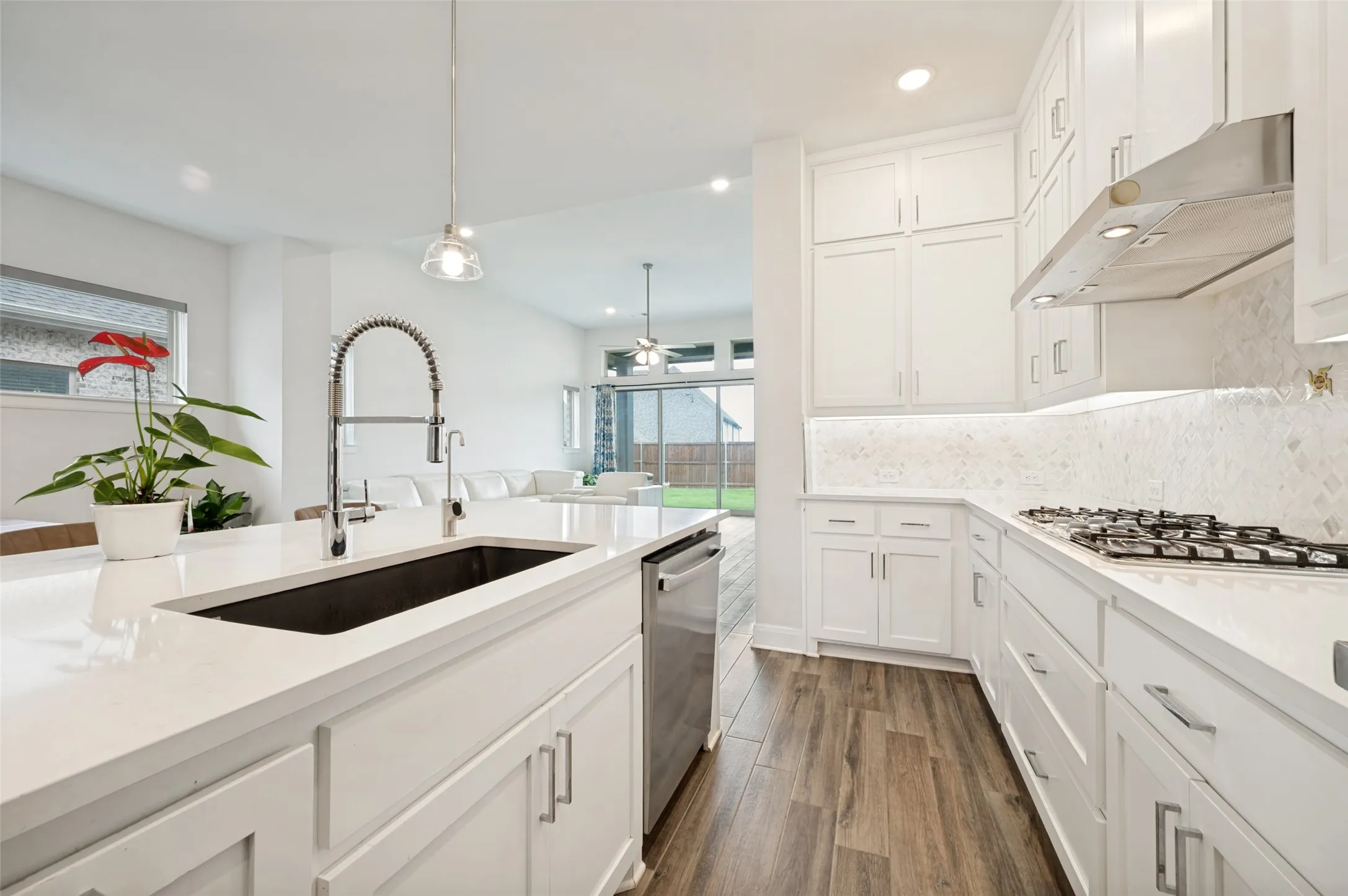 Gourmet kitchen featuring a large island with an undermount sink, stainless steel dishwasher, white cabinetry, a gas range, and wood-finish flooring