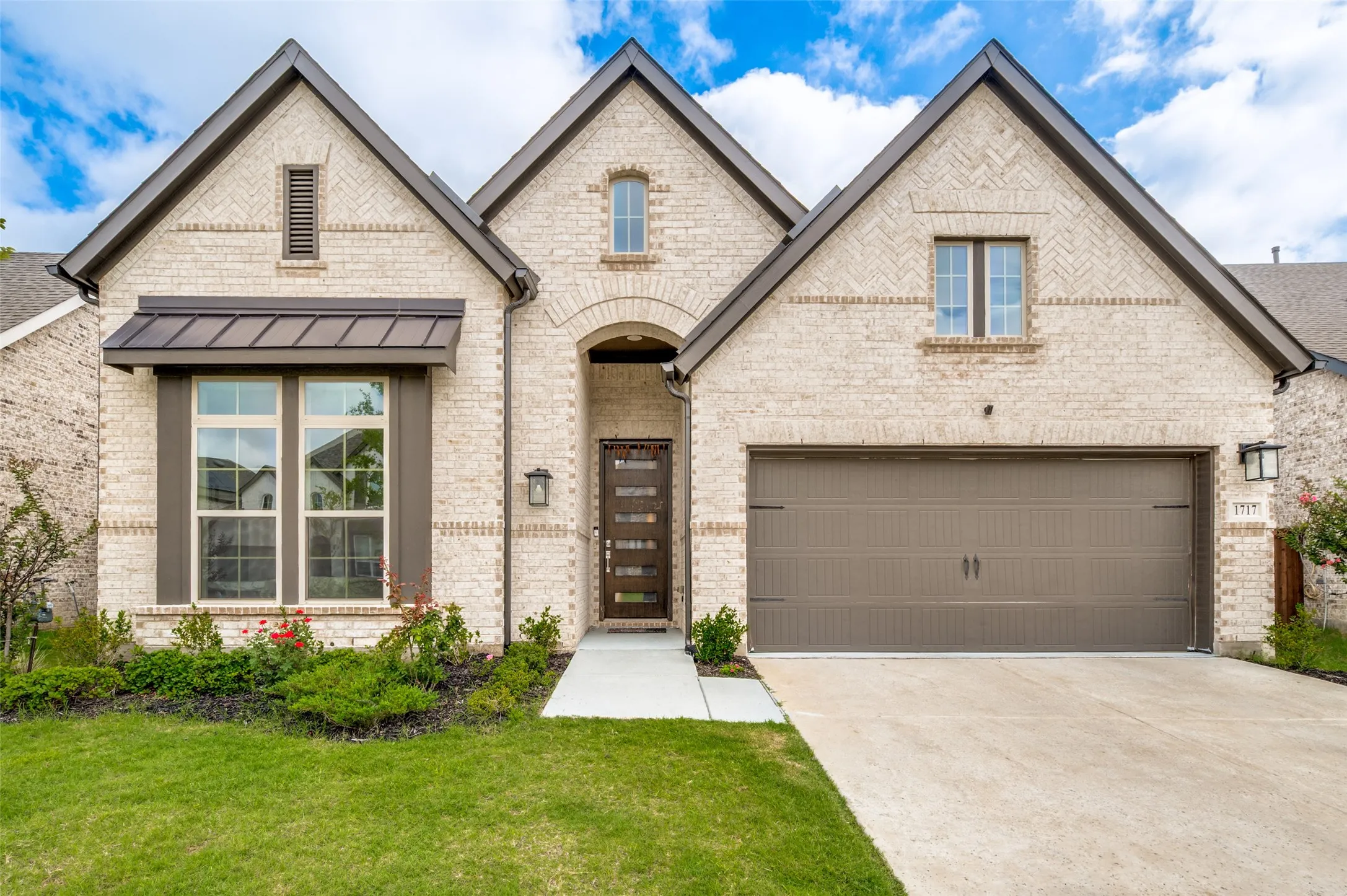 Light-colored brick exterior featuring gabled rooflines, dark trim, a two-car garage, an arched entry, and a contemporary front door