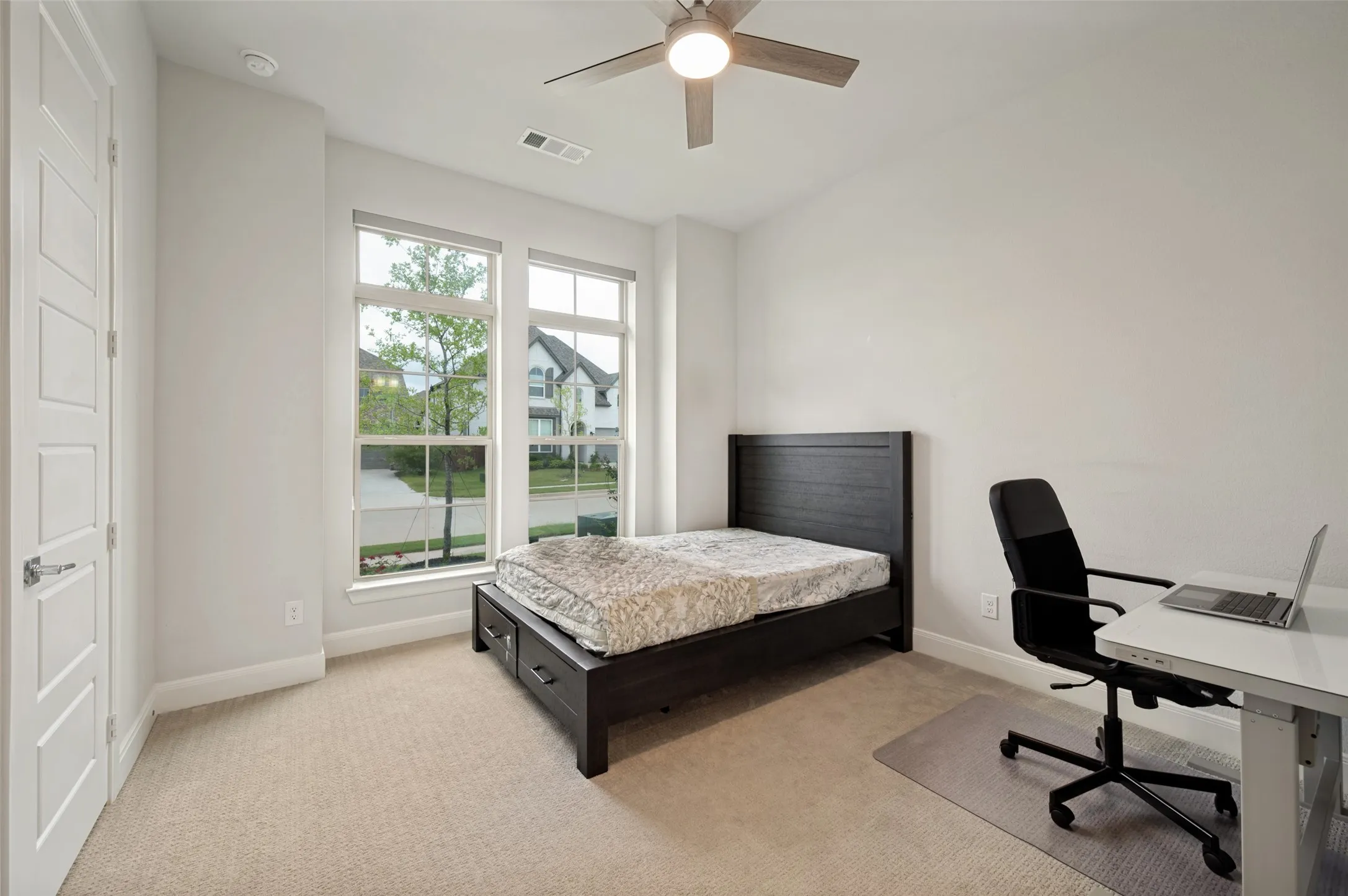 Bright room featuring two large windows, neutral carpeting, a ceiling fan with integrated lighting, and a five-panel interior door