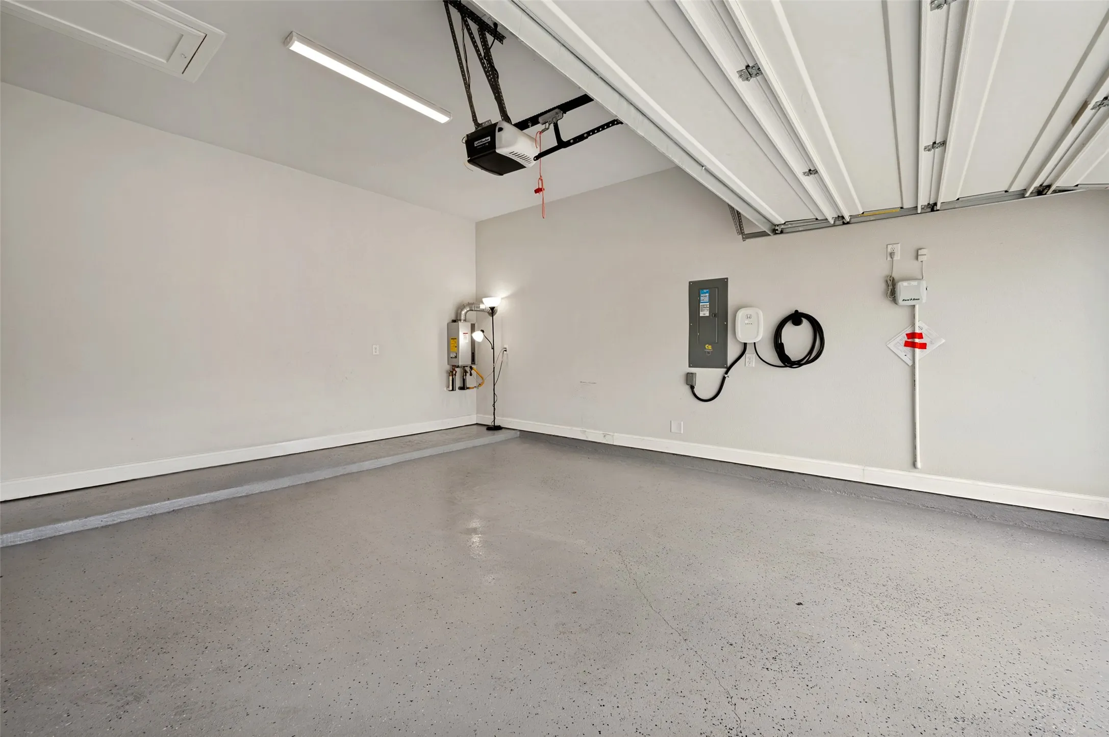 Spacious garage with epoxy-coated flooring, overhead fluorescent lighting, and an automatic garage door opener