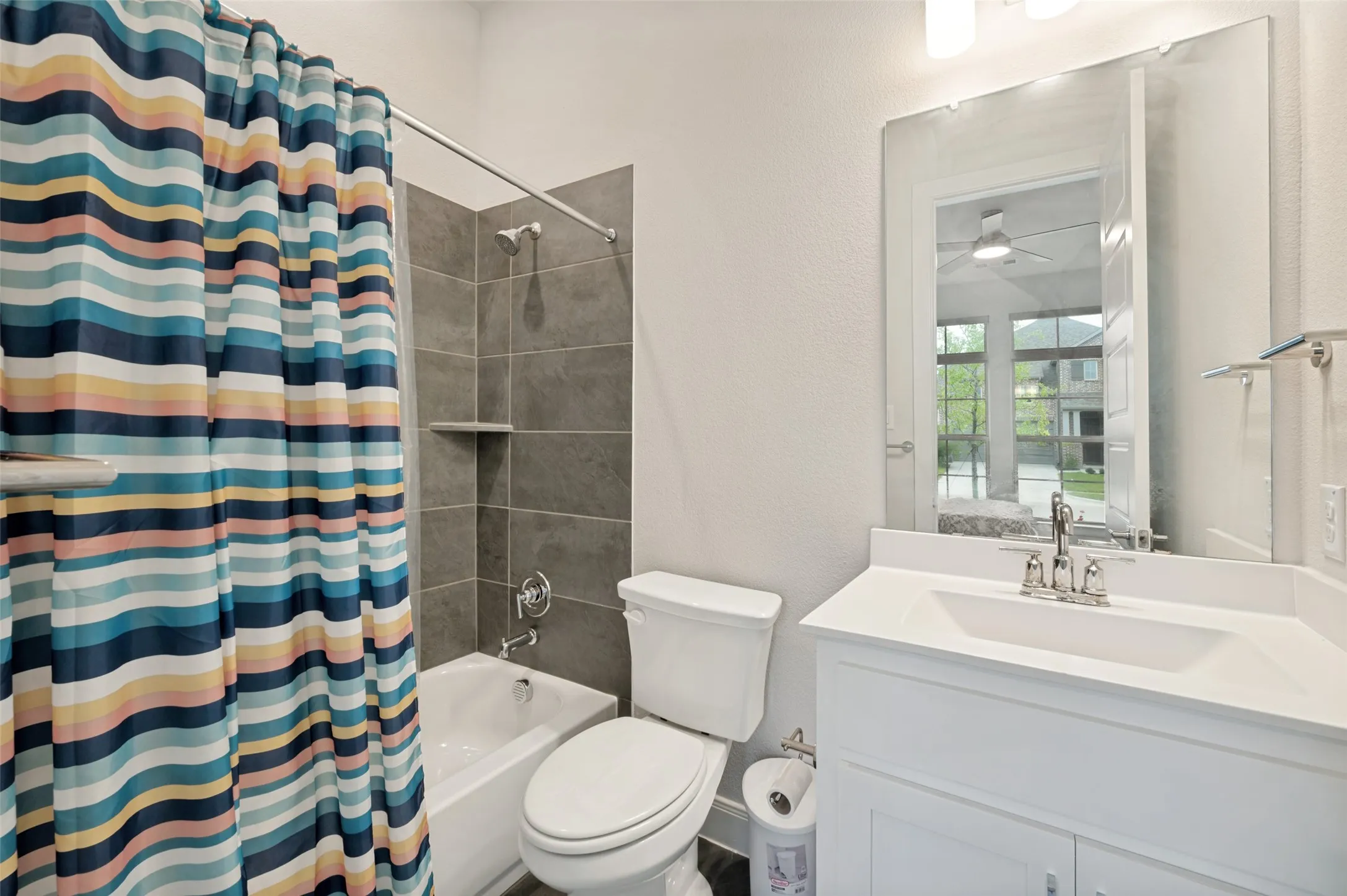 Full bathroom featuring a white vanity with an integrated sink, a white tub, and a shower with gray tile surround and built-in shelving