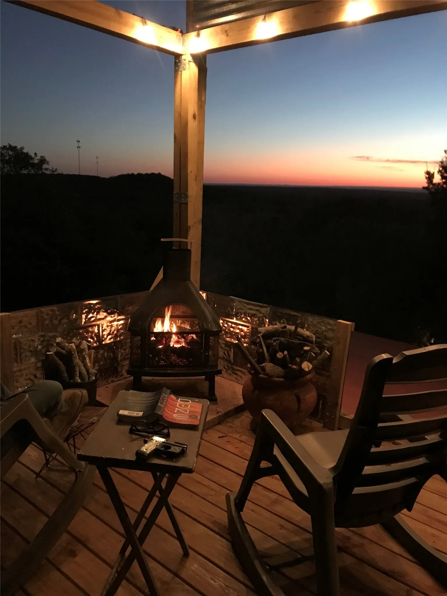 Wood-finish decking on an outdoor porch, featuring string lighting, a metal chiminea, and an open, expansive horizon