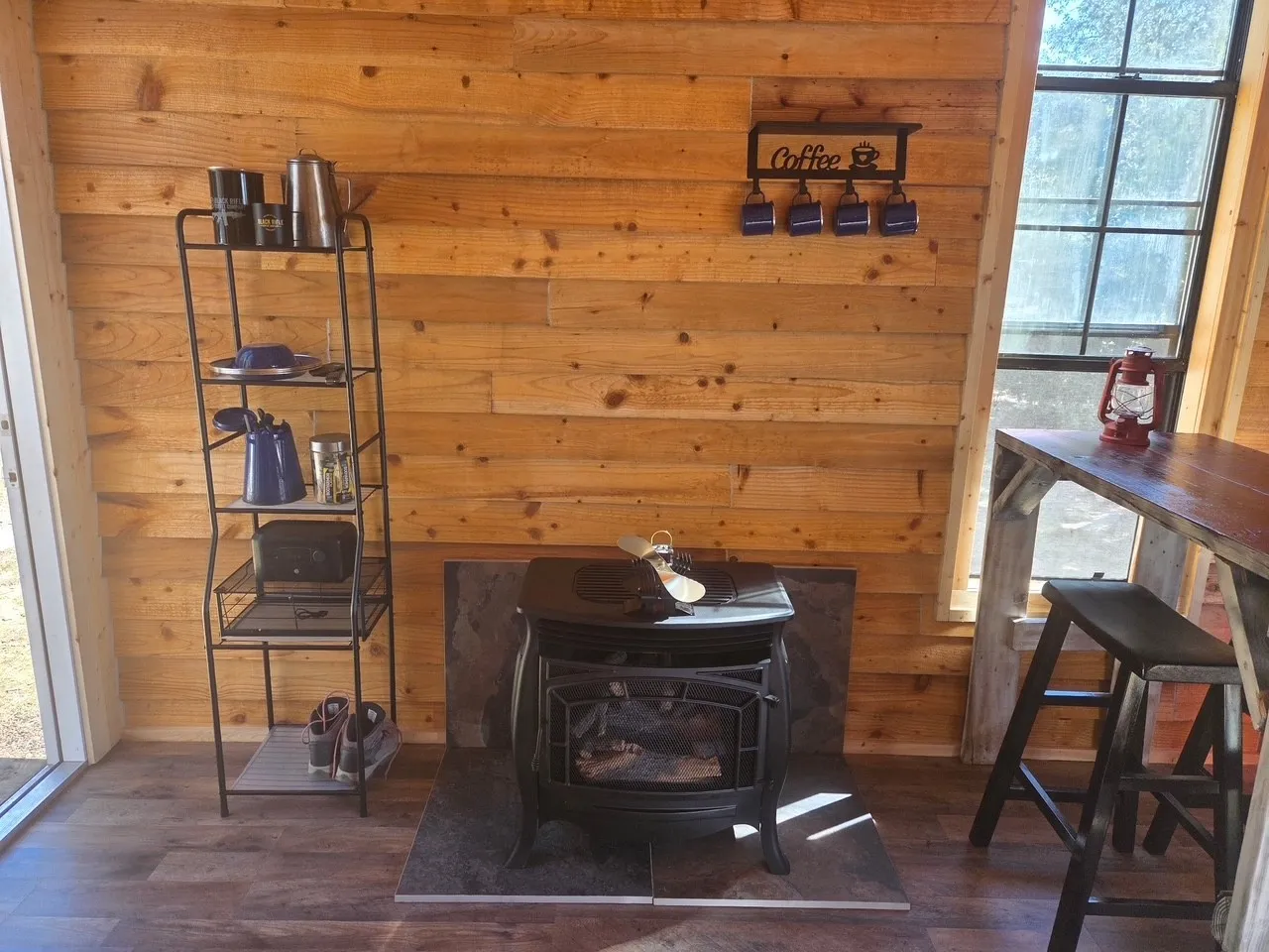Wood-paneled interior featuring a black cast-iron style stove on a dark tile hearth, wood-finish flooring, and a built-in wood bar with a stool
