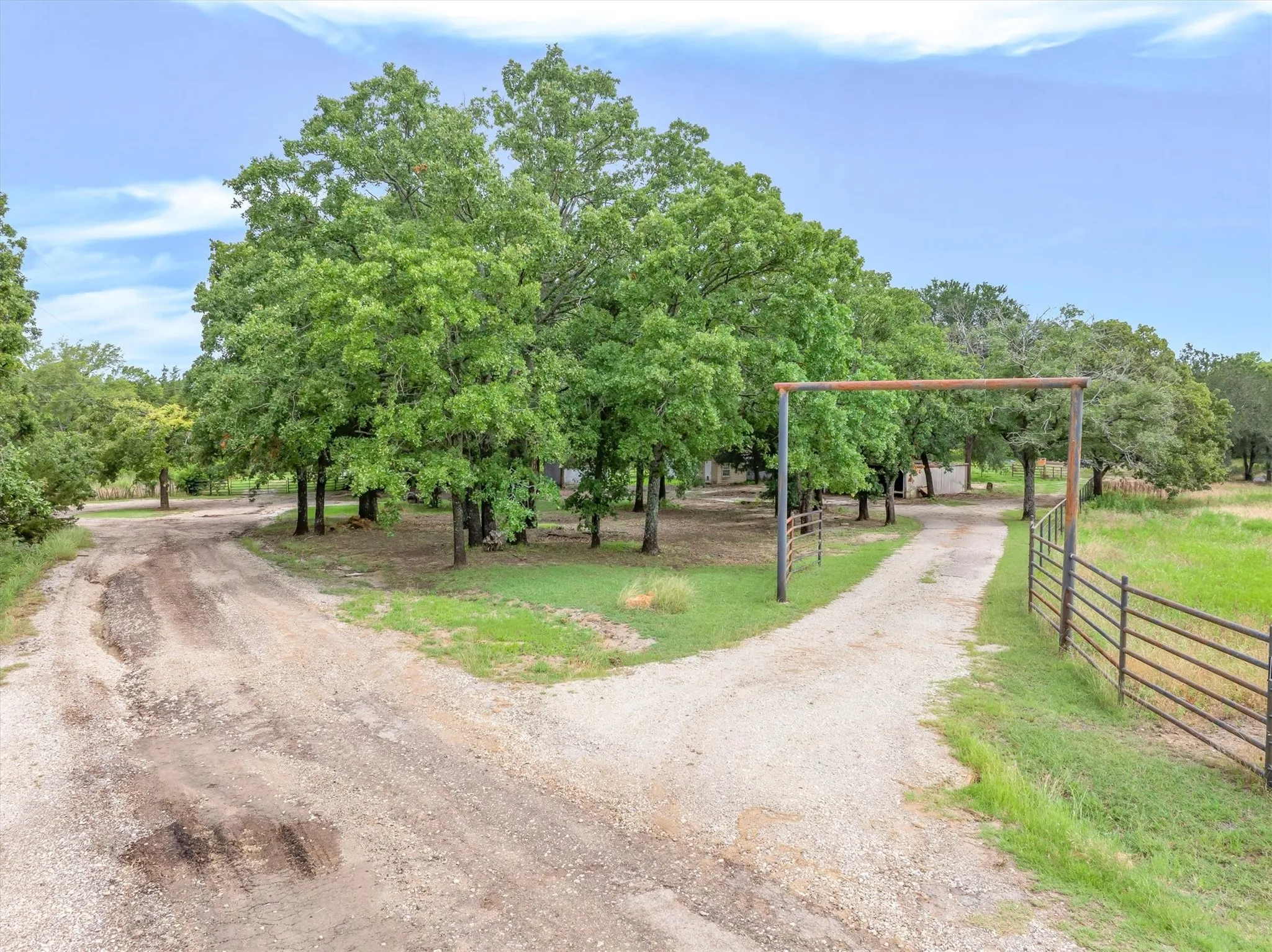 Split gravel driveway with mature trees and a metal gate framework