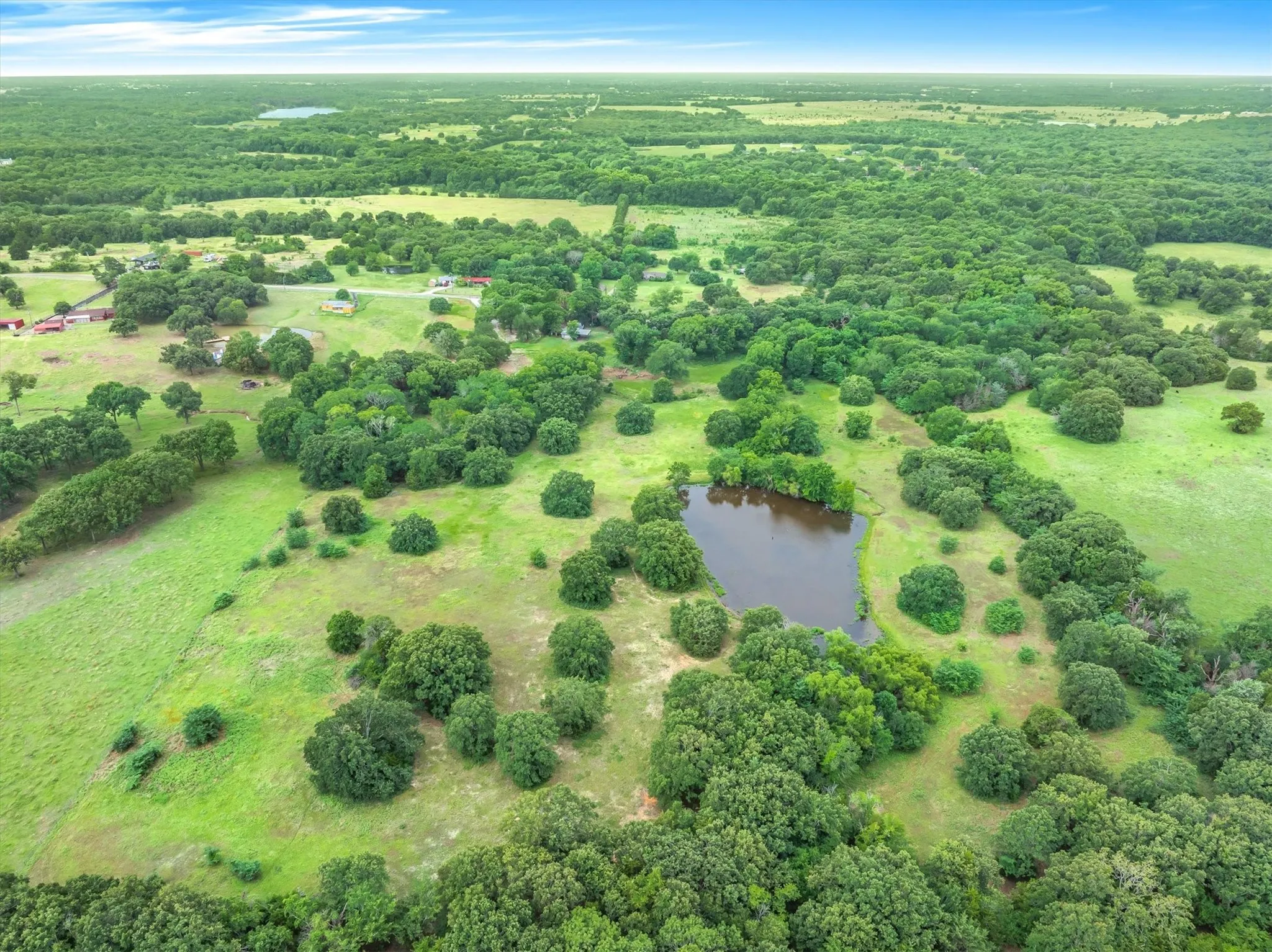 Expansive acreage featuring abundant mature trees, verdant green fields, and a prominent natural pond