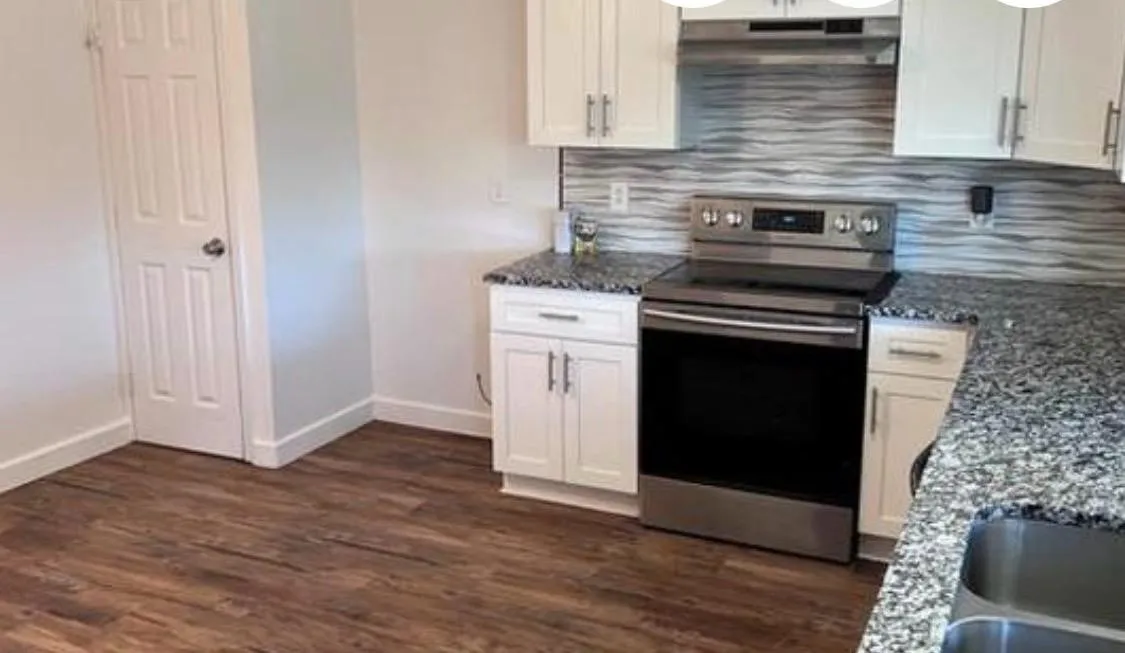 Kitchen featuring wood-finish flooring, white cabinetry with silver hardware, granite countertops, a stainless steel range, and a textured backsplash