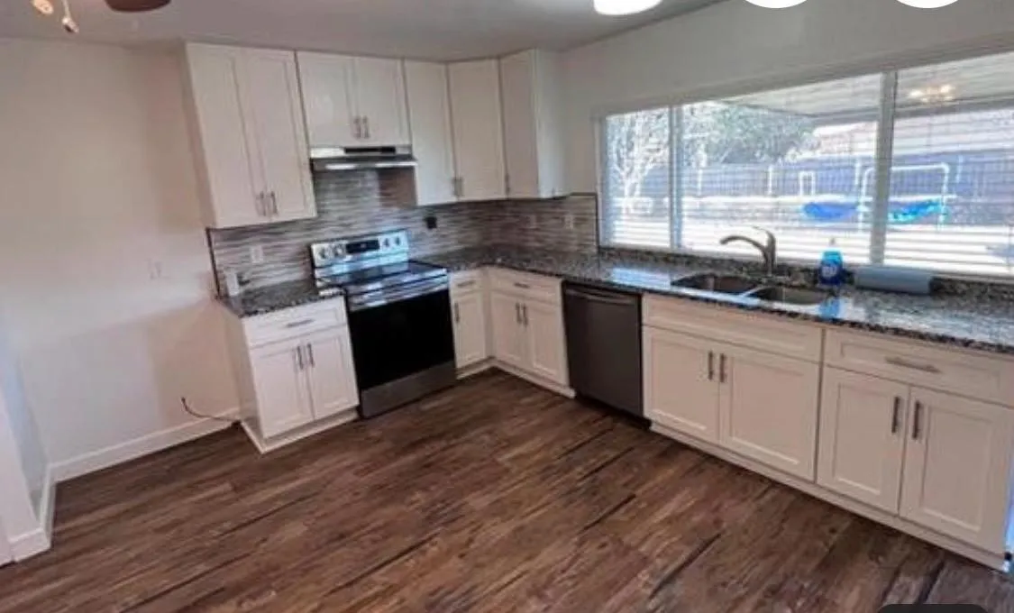Kitchen featuring white cabinetry, wood-finish flooring, stainless steel appliances, granite countertops, and a tiled backsplash