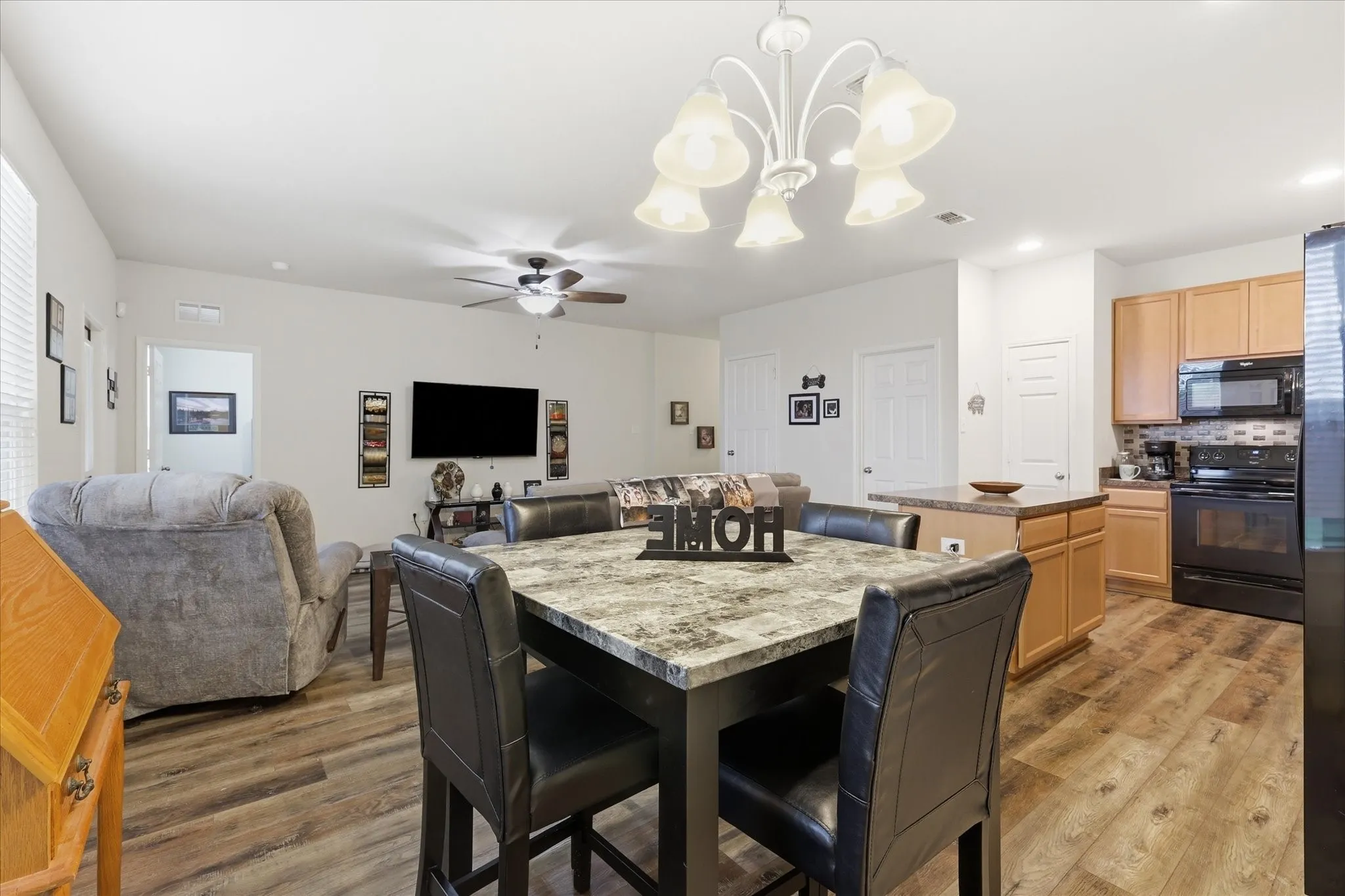 Open-concept living space featuring wood-finish flooring, a kitchen island with seating, natural wood cabinetry, and black appliances
