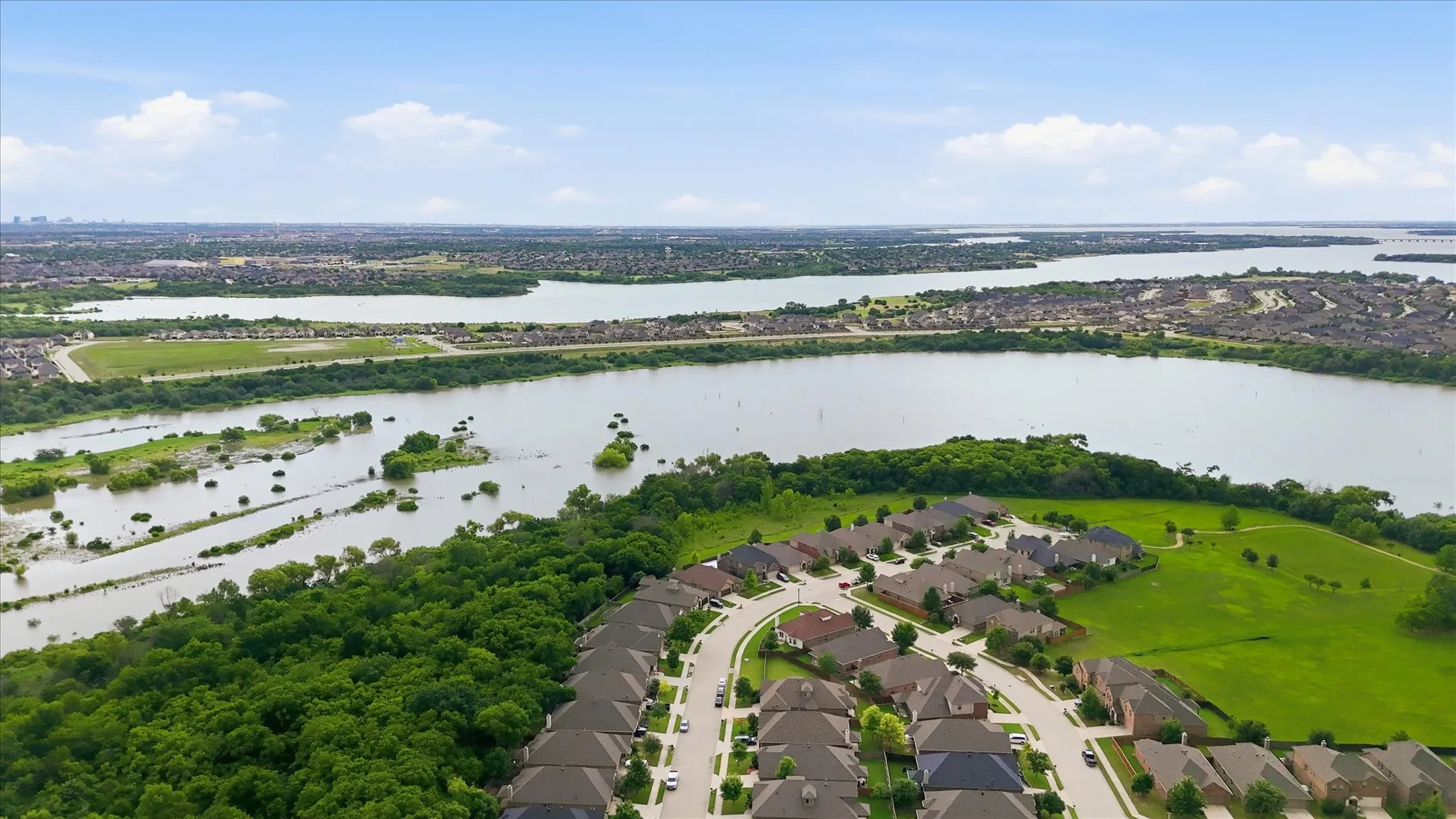 Expansive residential community with diverse home styles, bordered by significant water features and a lush green belt