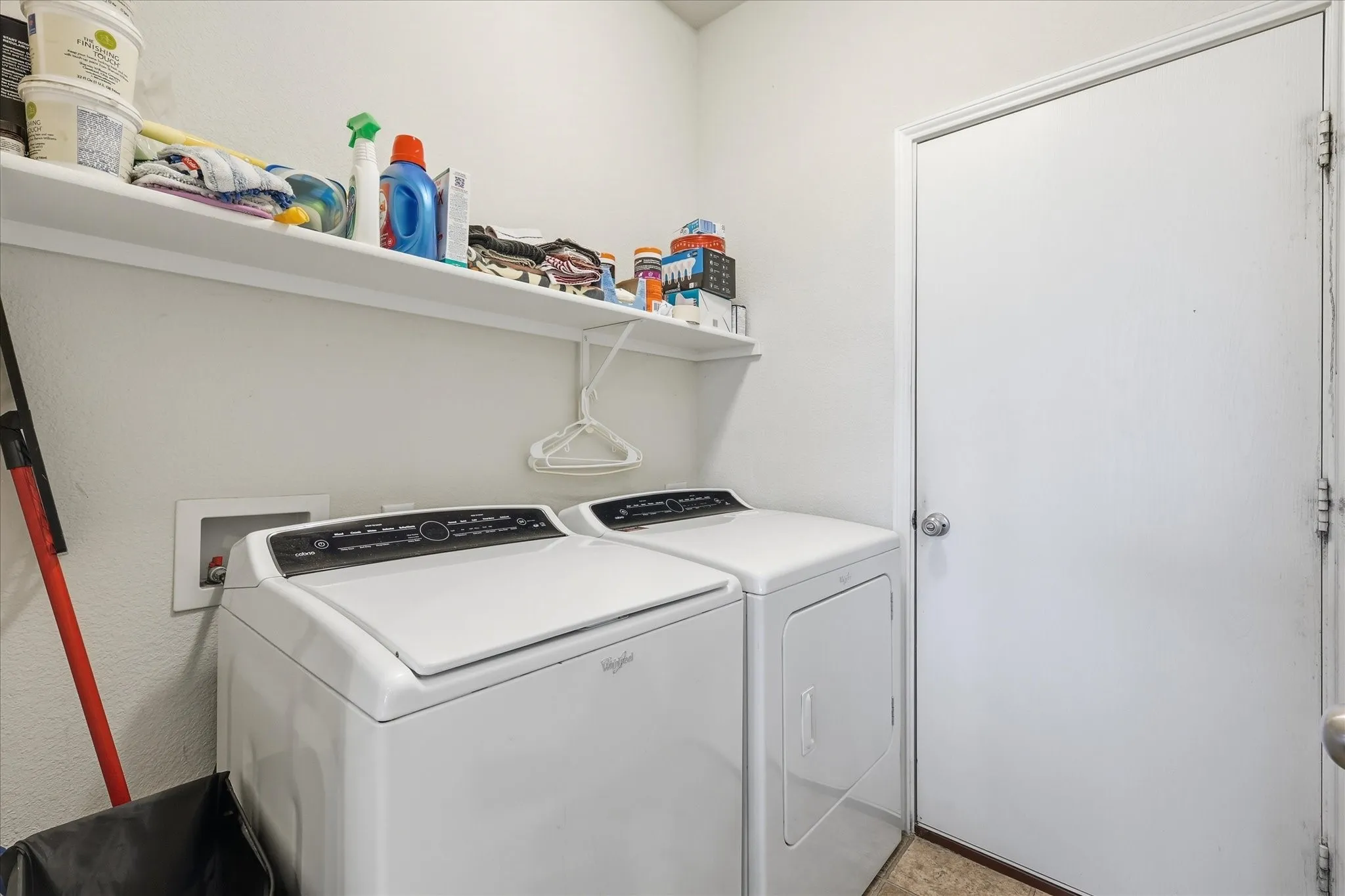 Dedicated laundry area featuring a white wall shelf, textured walls, and a white door with a round doorknob