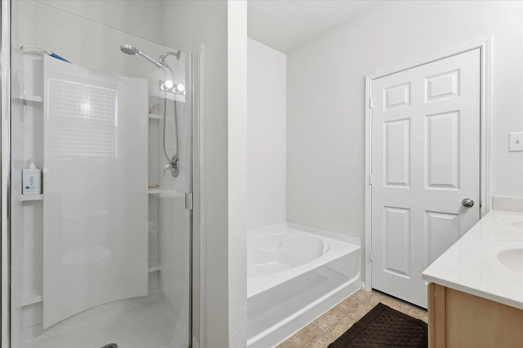 Bathroom featuring a glass-enclosed shower with a curved door, a built-in bathtub, a panel door, light-toned wood-finish cabinetry, and a light countertop with an integrated sink
