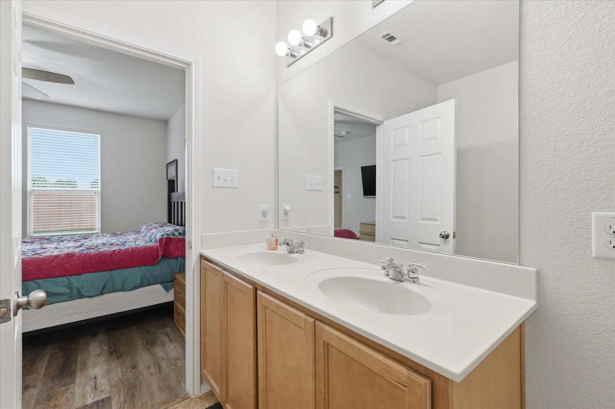 Bathroom vanity featuring dual undermount sinks with chrome fixtures, a spacious countertop, and light wood-finish cabinetry