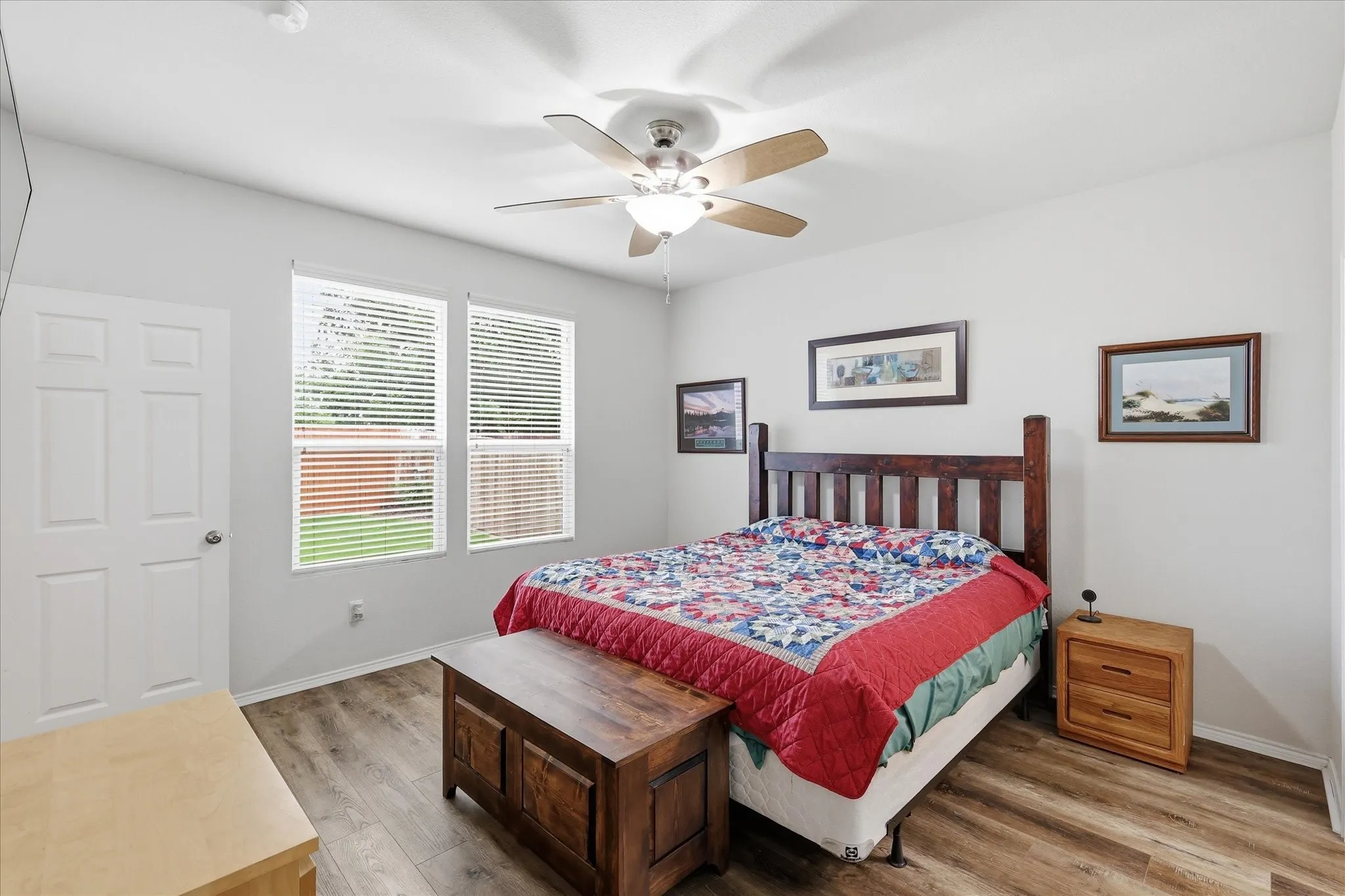 Spacious room featuring wood-finish flooring, two large windows with blinds, and a ceiling fan with integrated lighting