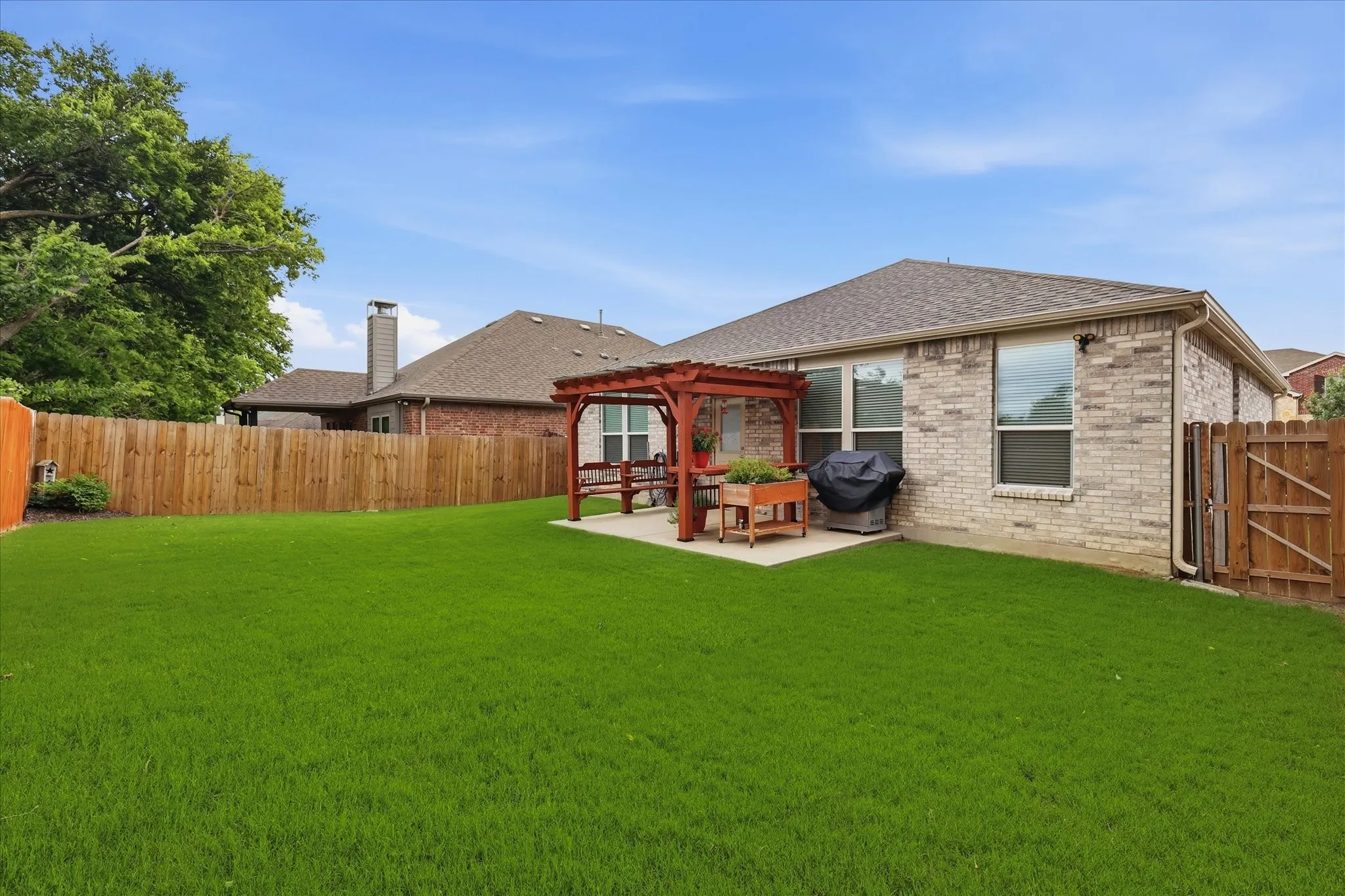 Expansive backyard featuring a lush lawn, privacy fencing, and a red wood pergola over a concrete patio
