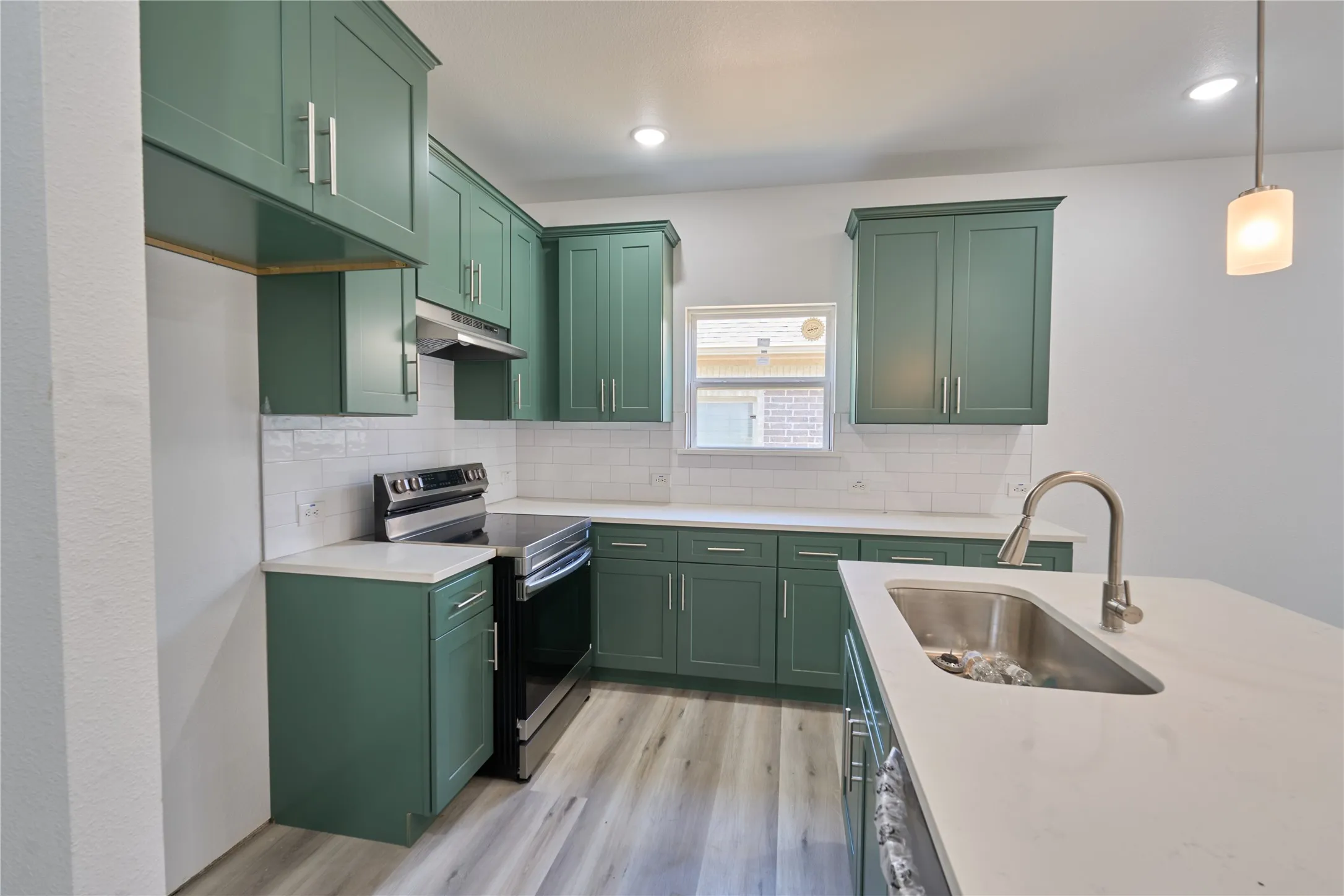 Kitchen featuring green shaker-style cabinetry, white countertops, wood-finish flooring, a stainless steel sink with a gooseneck faucet, and white subway tile backsplash