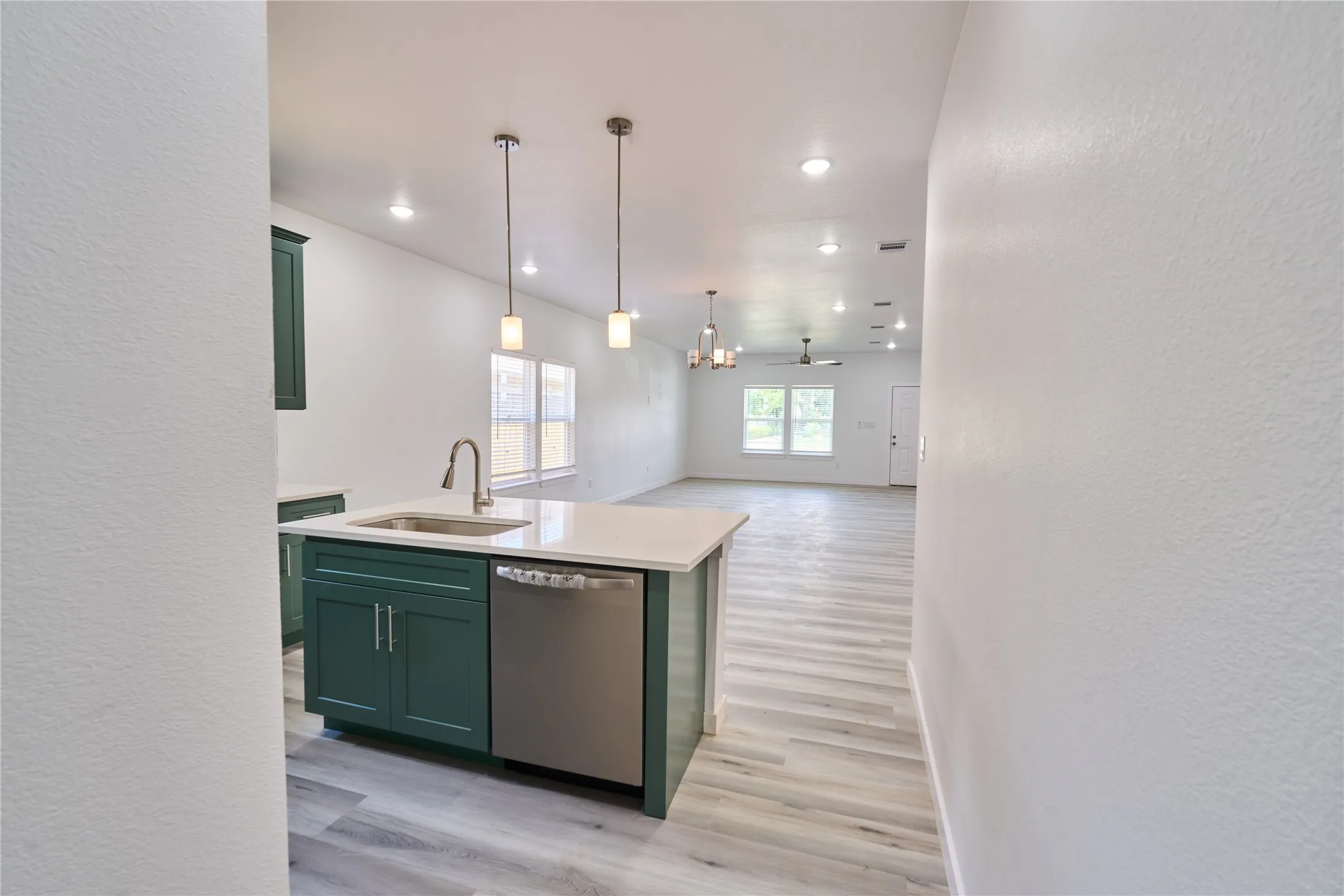 Kitchen island featuring a stainless steel sink with a high-arc faucet, integrated dishwasher, and pendant lighting