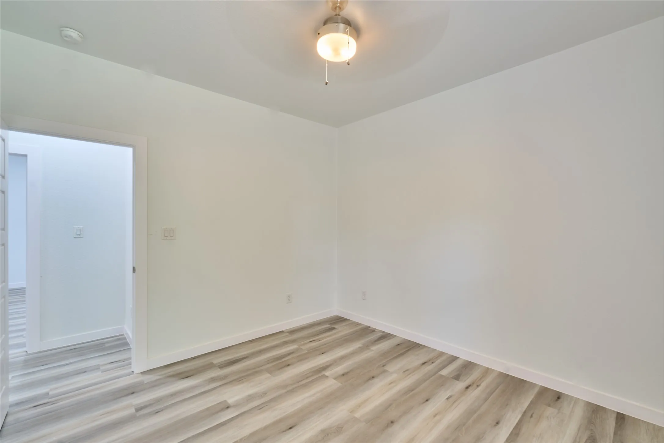 Interior room featuring light wood-finish flooring, white walls, and a ceiling fan with integrated lighting