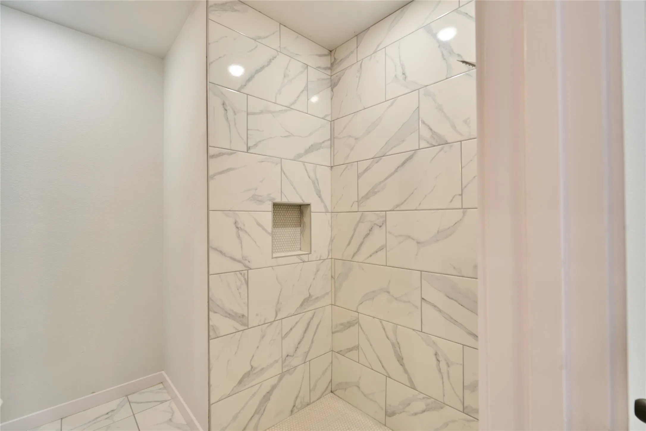 Shower enclosure featuring white marble-look subway tile walls, a built-in shower niche, and a white penny tile floor