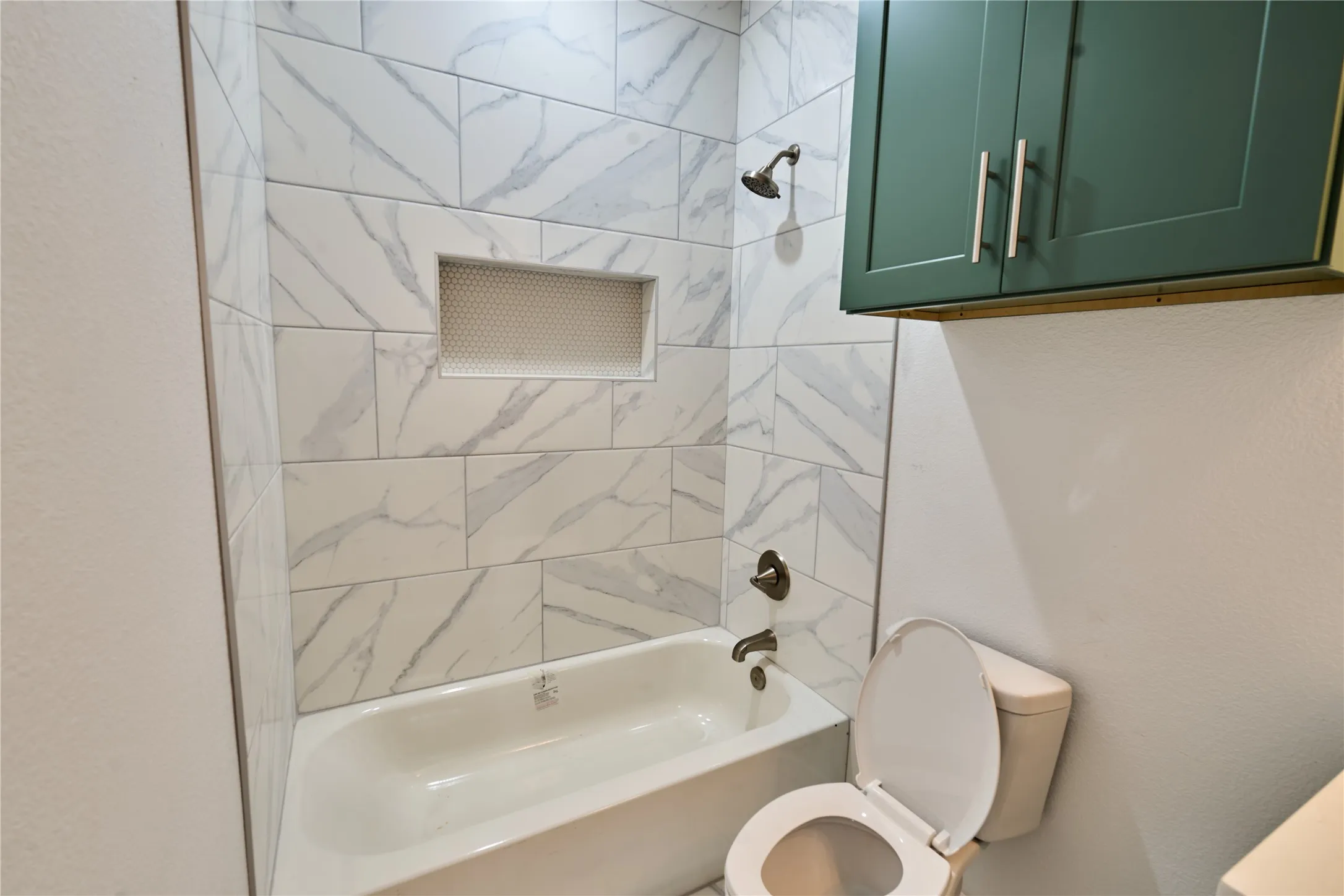 Bathroom featuring a bathtub with subway tile surround, recessed shower niche, oil-rubbed bronze shower fixtures, and green wall cabinetry with silver hardware