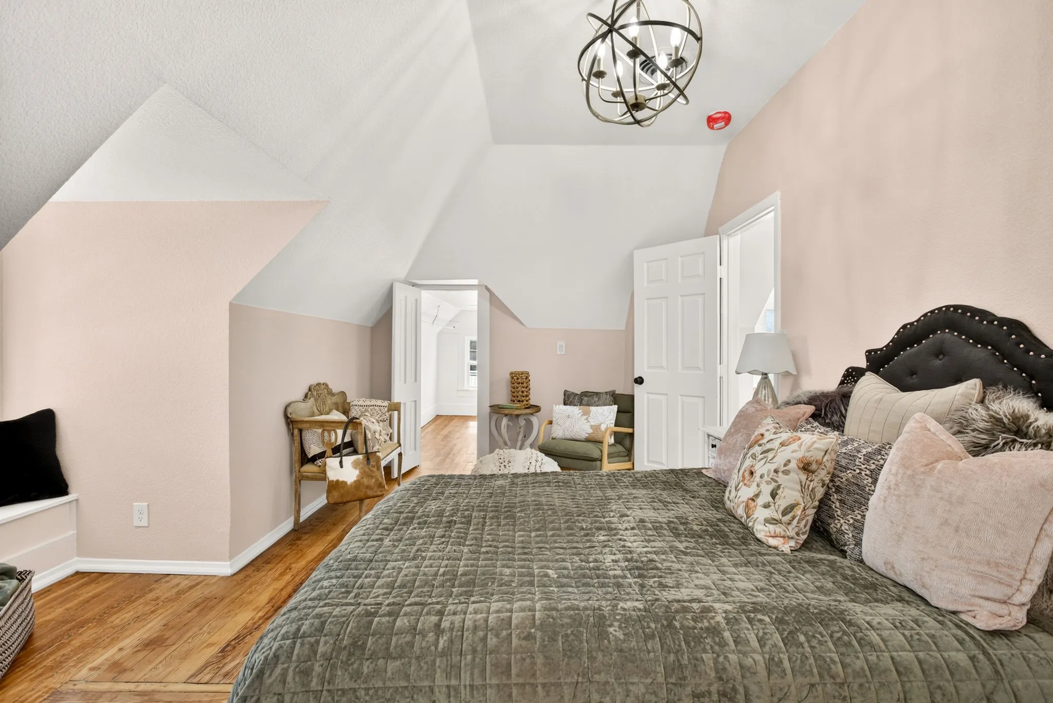 Attic bedroom featuring pitched ceilings, wood-finish flooring, a built-in window bench, and an ornate spherical chandelier