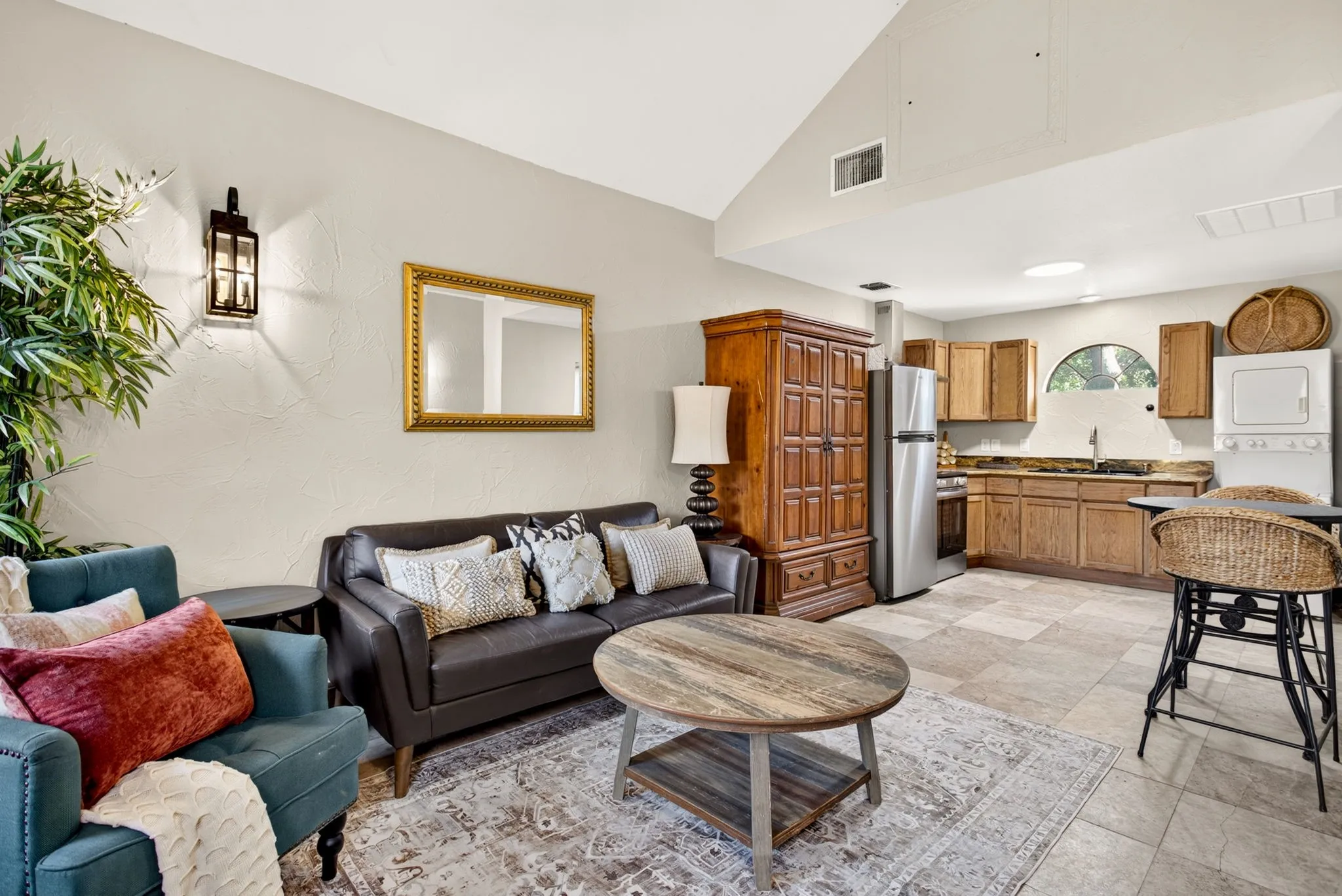 Open-concept liviceilings, tile and a kitchen area with wood cabinetry, stainless steel appliances, and a stacked washer/dryer unit