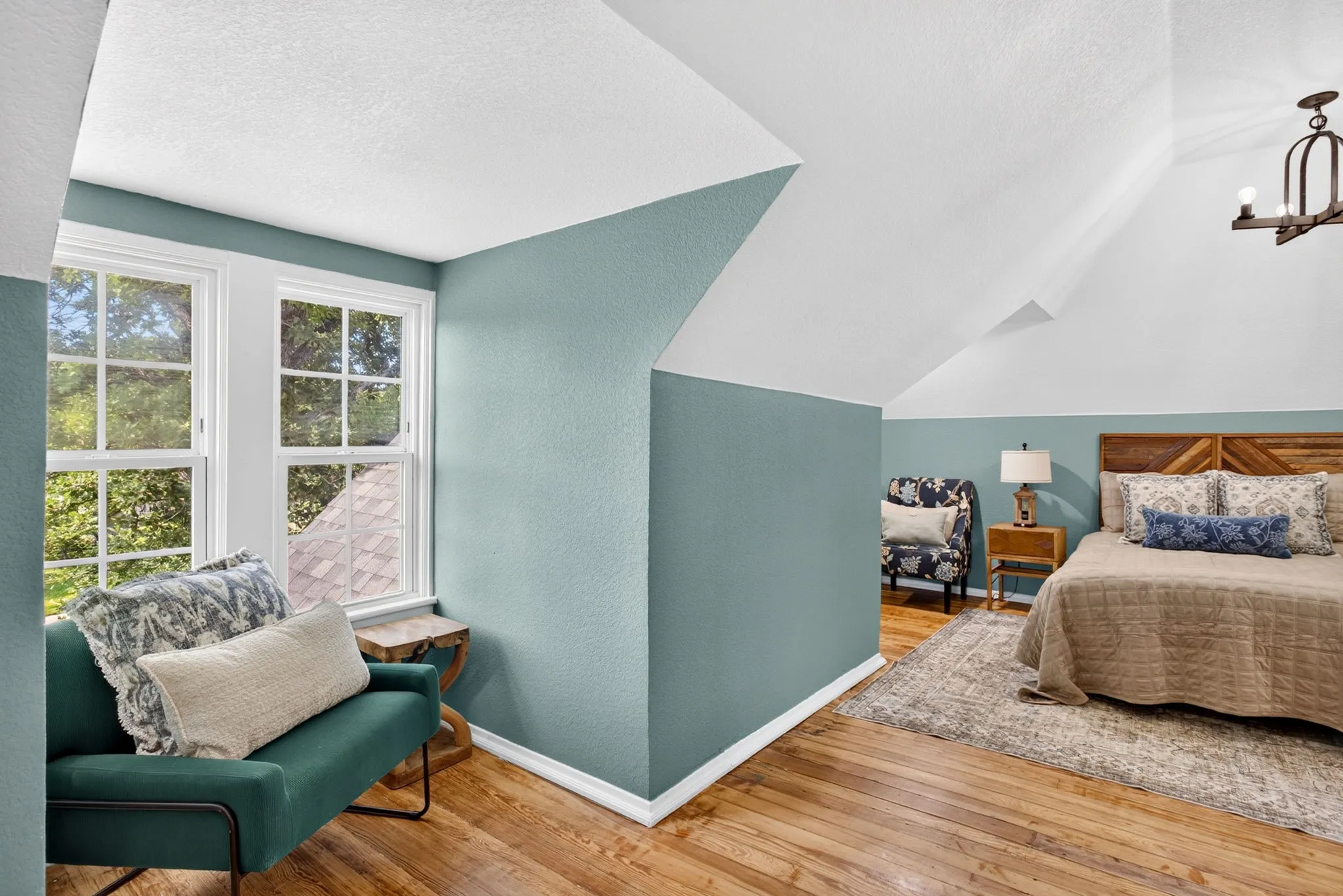 Spacious room featuring wood-finish flooring, two large windows, sloped ceilings, and a decorative ceiling light fixture