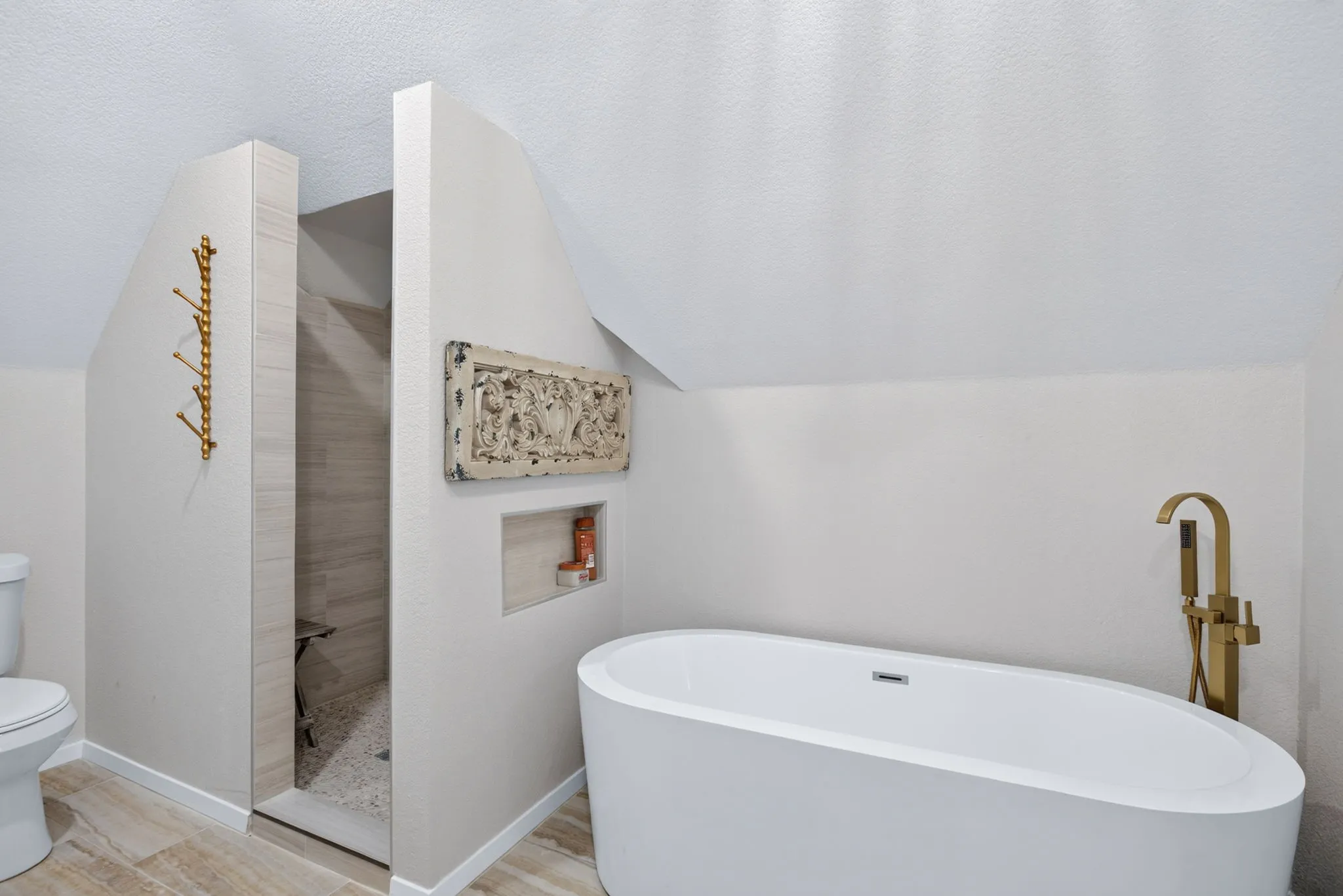 Bathroom featuring a freestanding white soaking tub with a brass floor-mounted faucet, a walk-in shower with tiled walls and a built-in bench, and wood-finish tile flooring