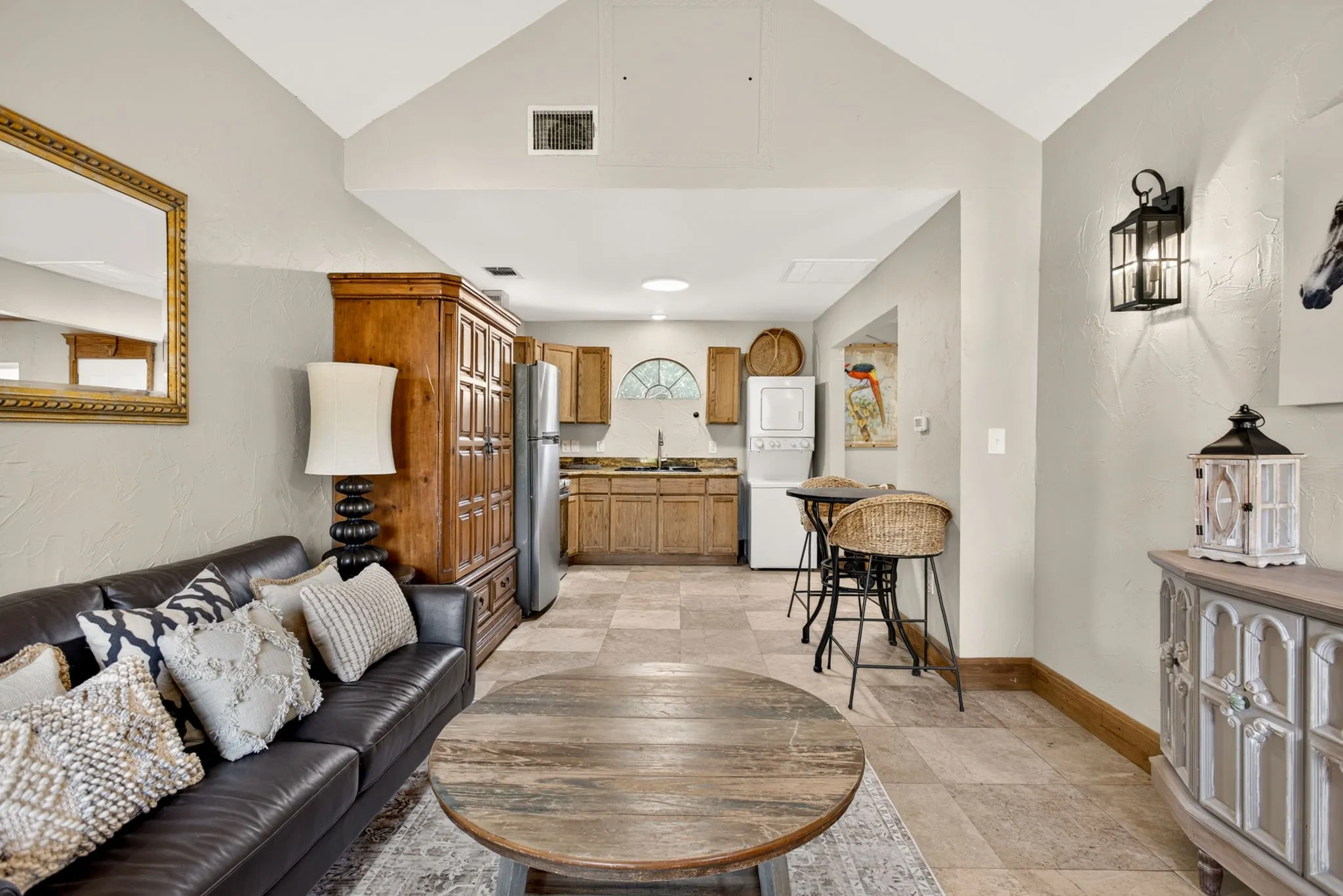 Vaulted ceiling space featuring a kitchenette with wood-finish cabinetry, stainless steel refrigerator, and a stackable washer and dryer