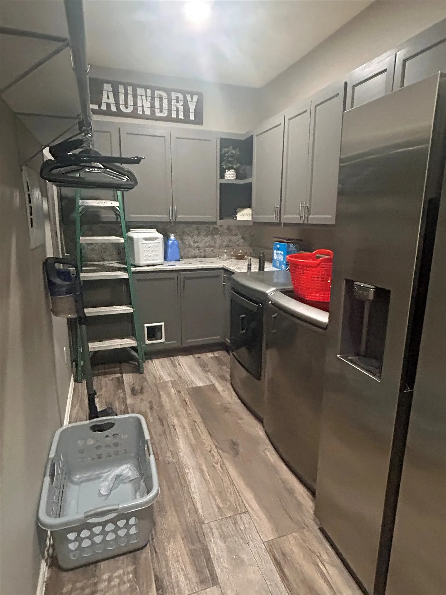 Laundry room featuring wood-finish flooring, gray cabinetry, a stone-look backsplash, and a built-in hanging rod