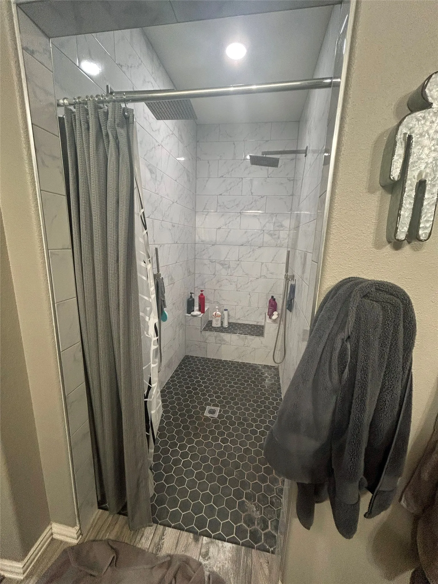 Spacious walk-in shower featuring gray hexagonal floor tiles and white subway-style wall tiles