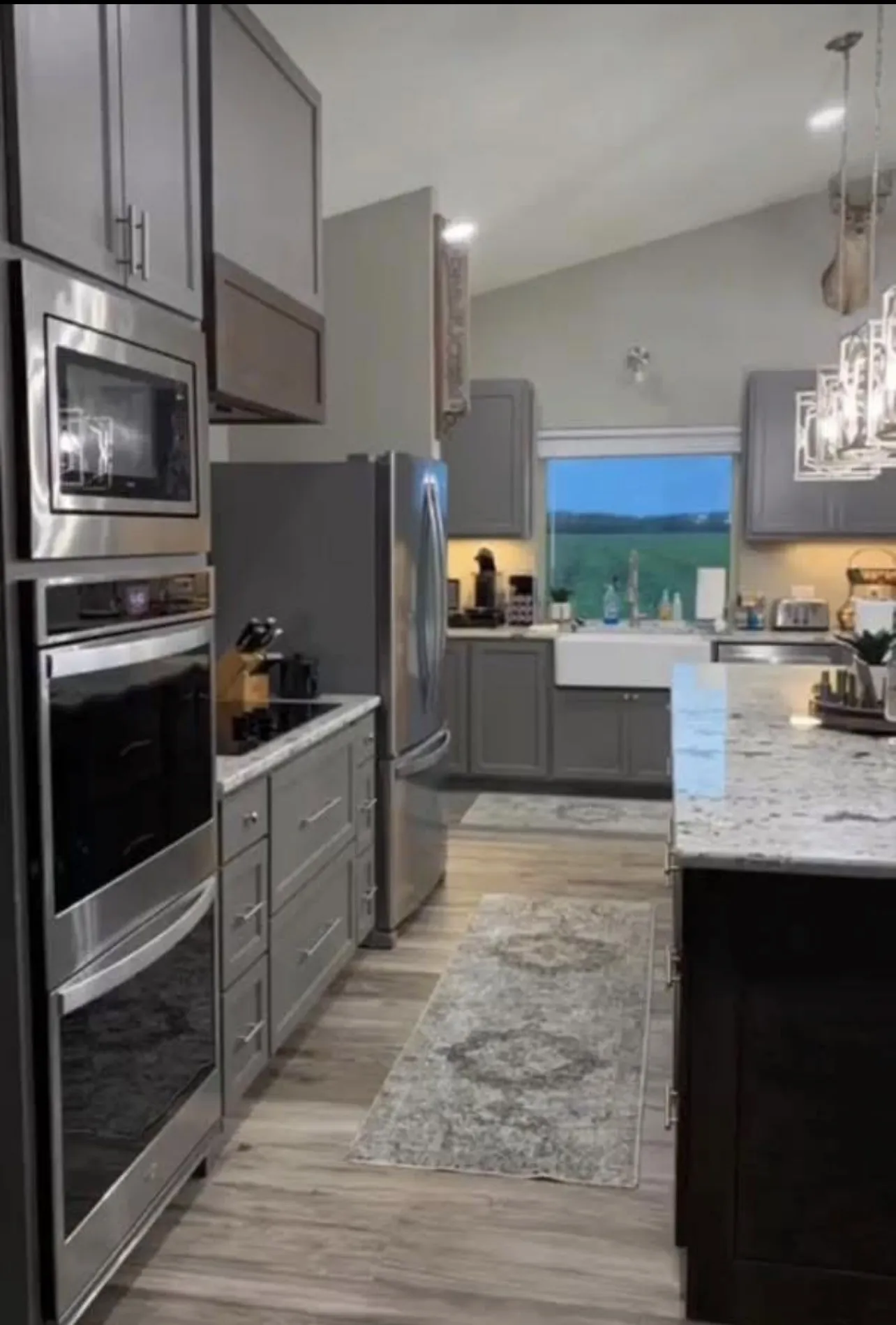 Modern kitchen featuring stainless steel appliances, grey cabinetry, wood-finish flooring, and a vaulted ceiling