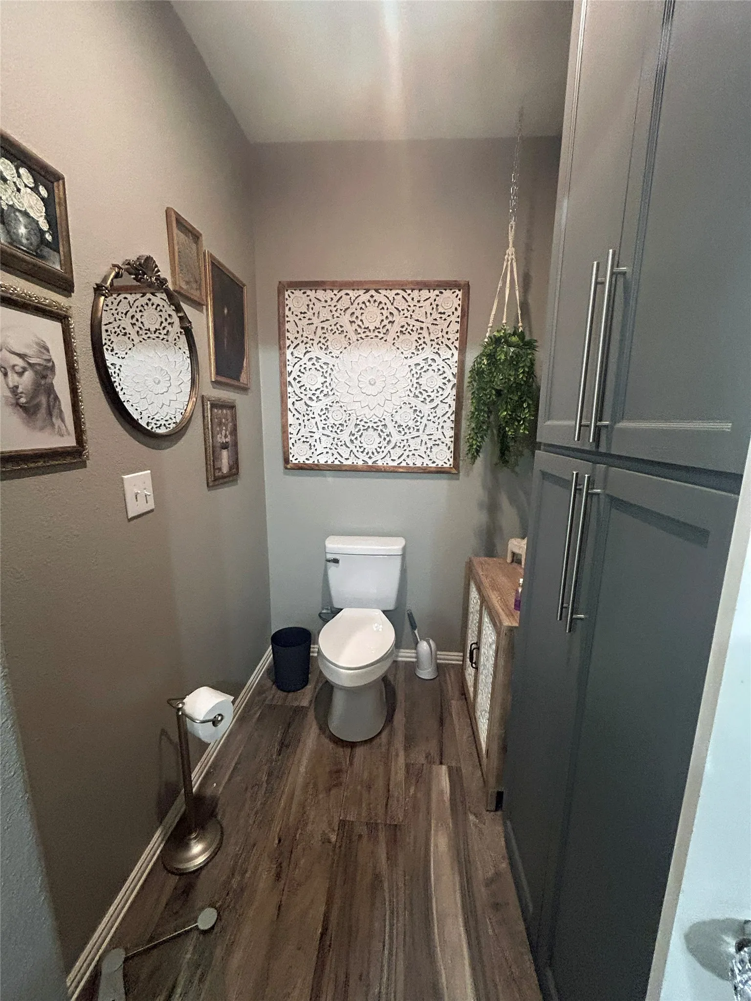Powder room with wood-finish flooring, white baseboards, and built-in gray cabinetry featuring brushed nickel hardware