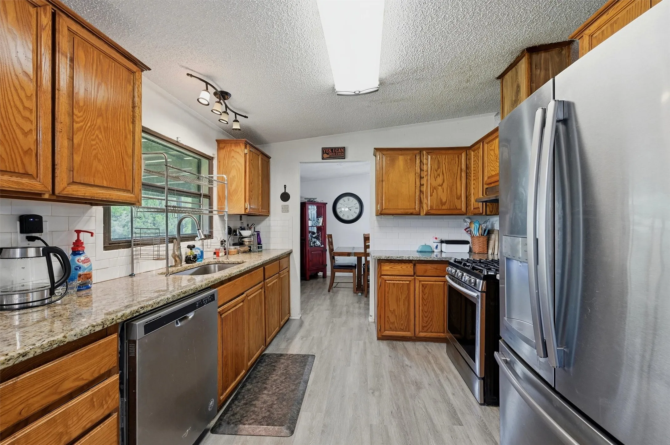 Galley kitchen featuring wood cabinetry, granite countertops, and stainless steel appliances