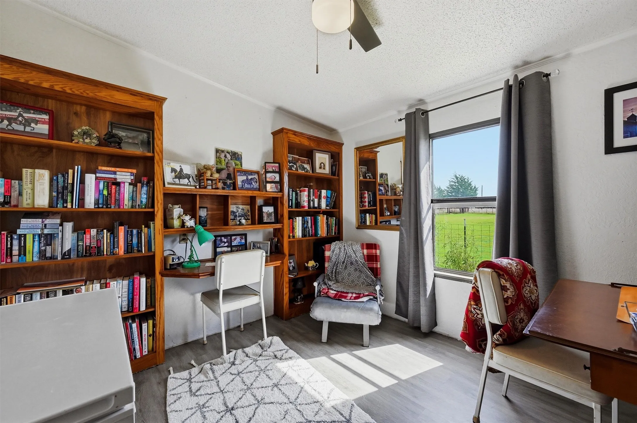 Interior room featuring wood-finish flooring, two built-in wood bookshelves, a window with exterior field scenery, and a ceiling fan