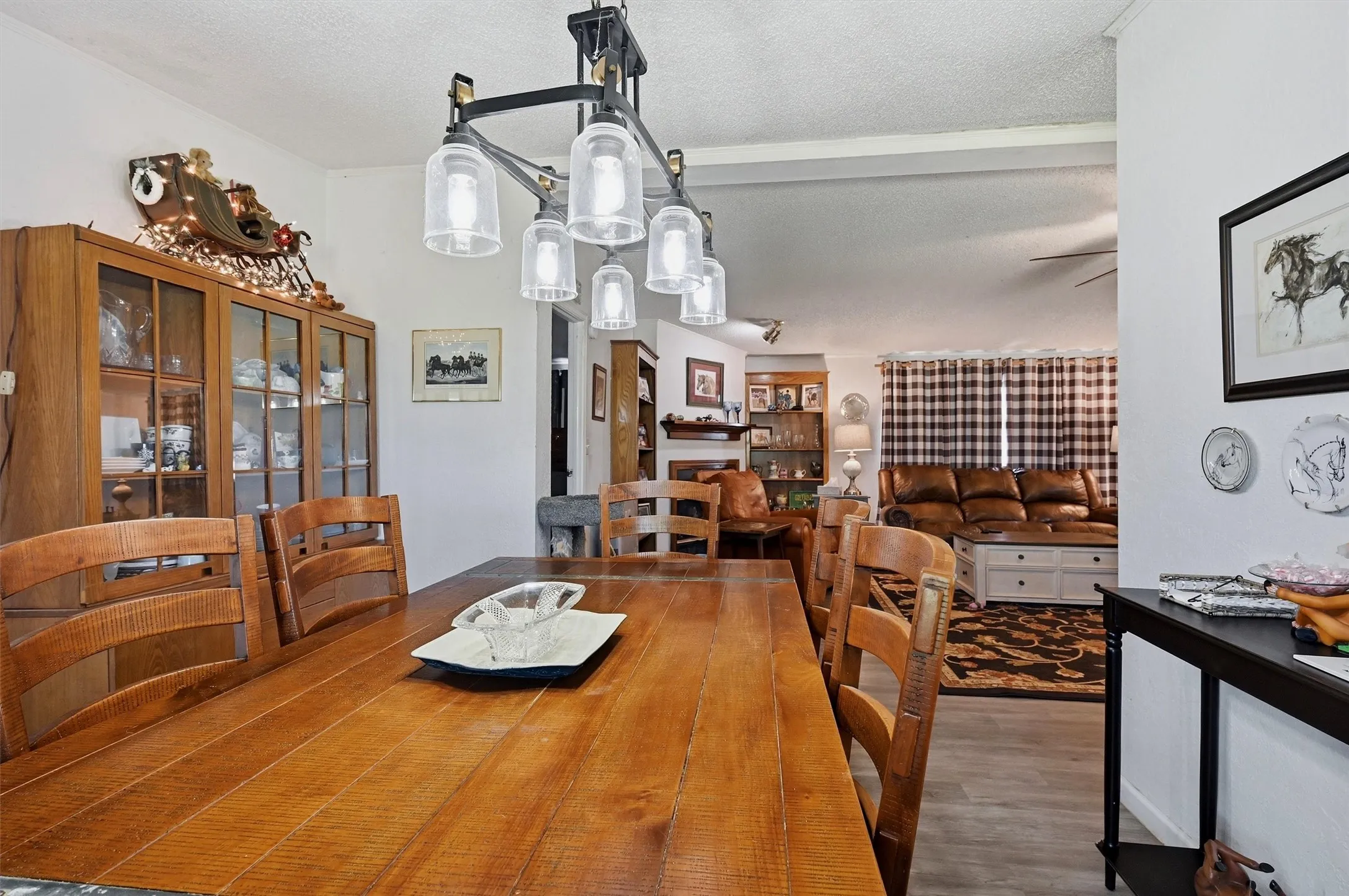 Open-concept dining and living areas feature a linear chandelier with clear glass shades, and a built-in wood display cabinet