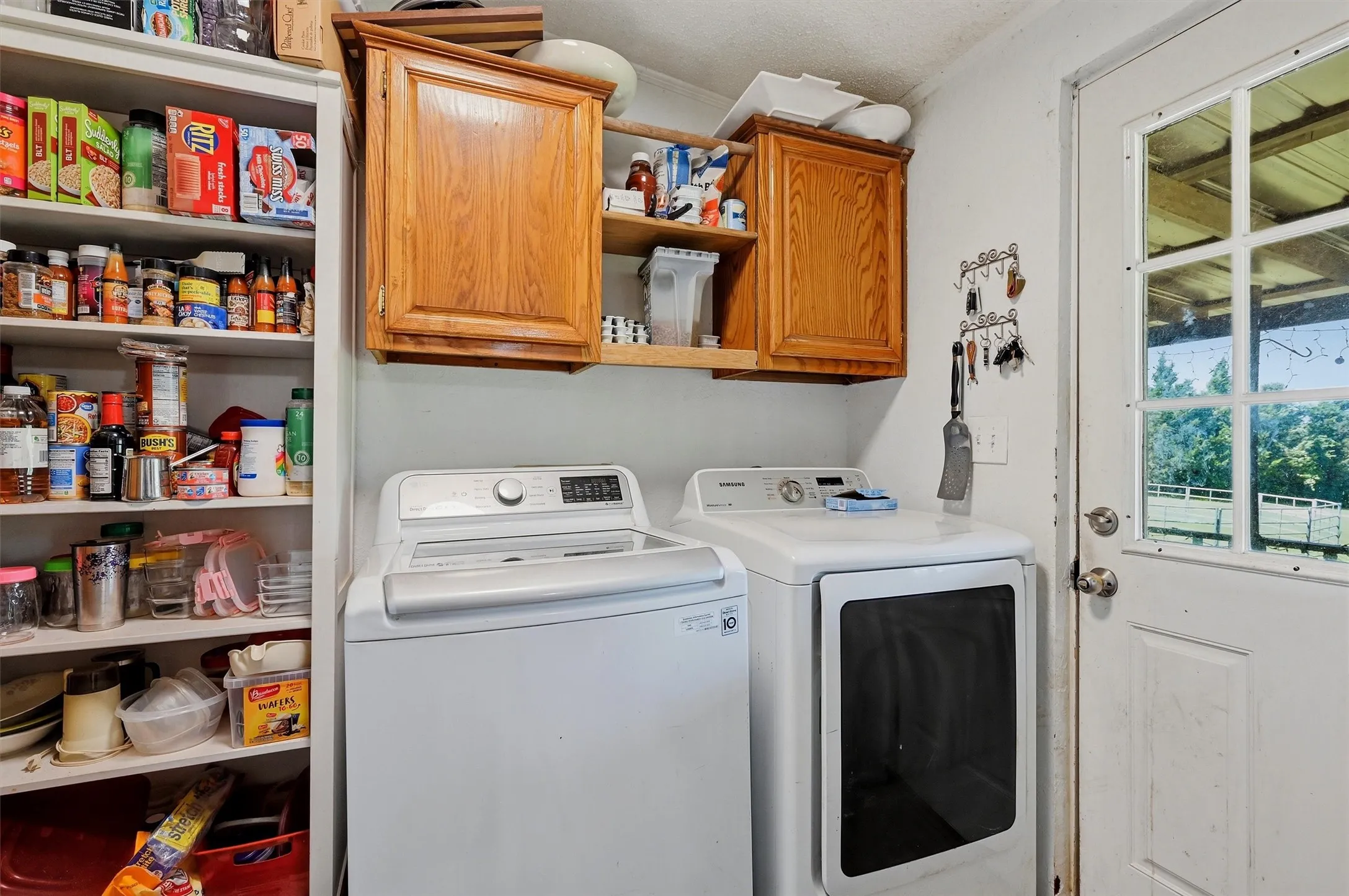 Dedicated laundry area featuring overhead wood-finish cabinetry, a full-height built-in shelving unit, and a glass-paneled exterior door